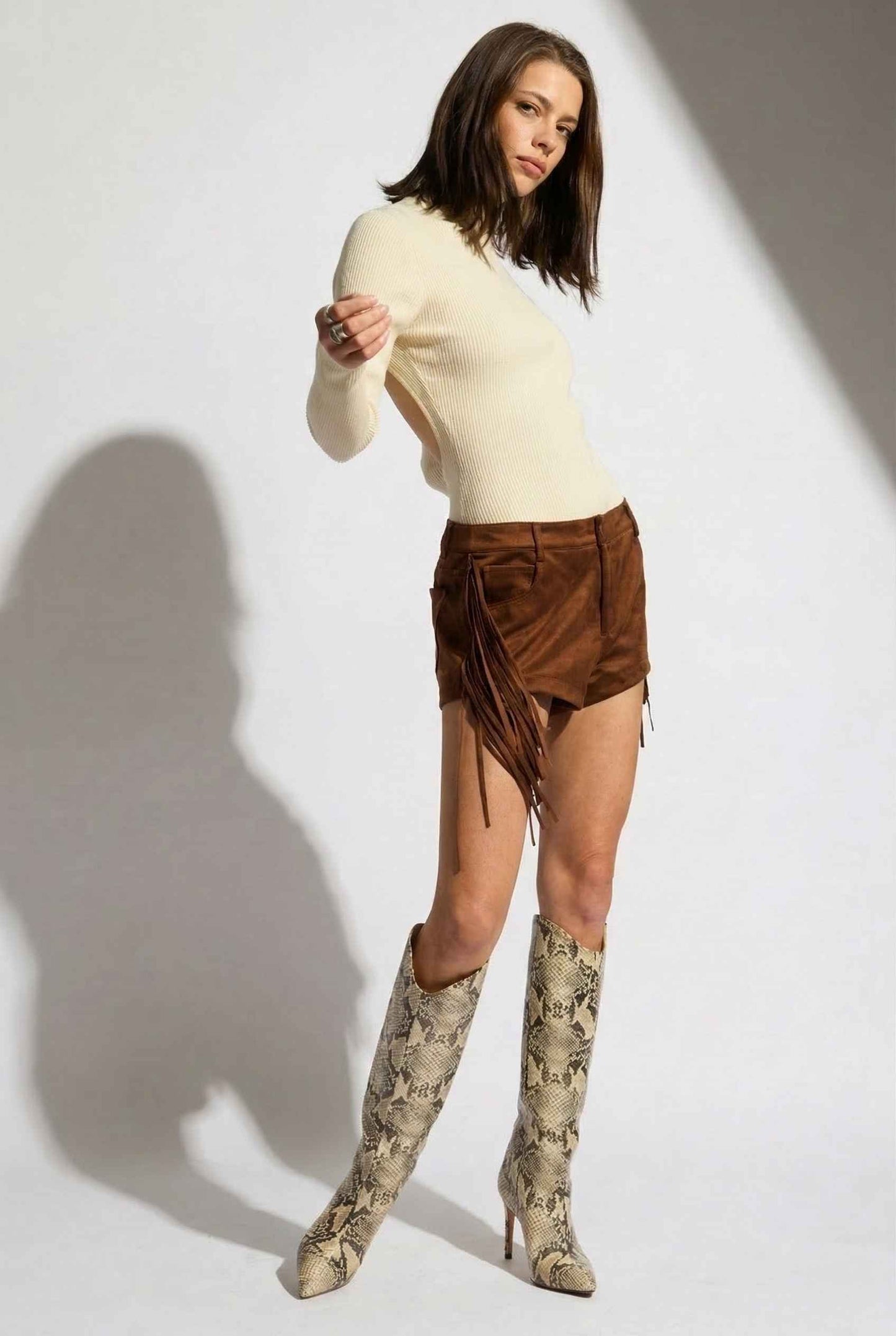 Model wearing Kiera Bodysuit Ribbed Knit Turtleneck Long Sleeve Bodysuit in Ivory with suede shorts and tall snake boots