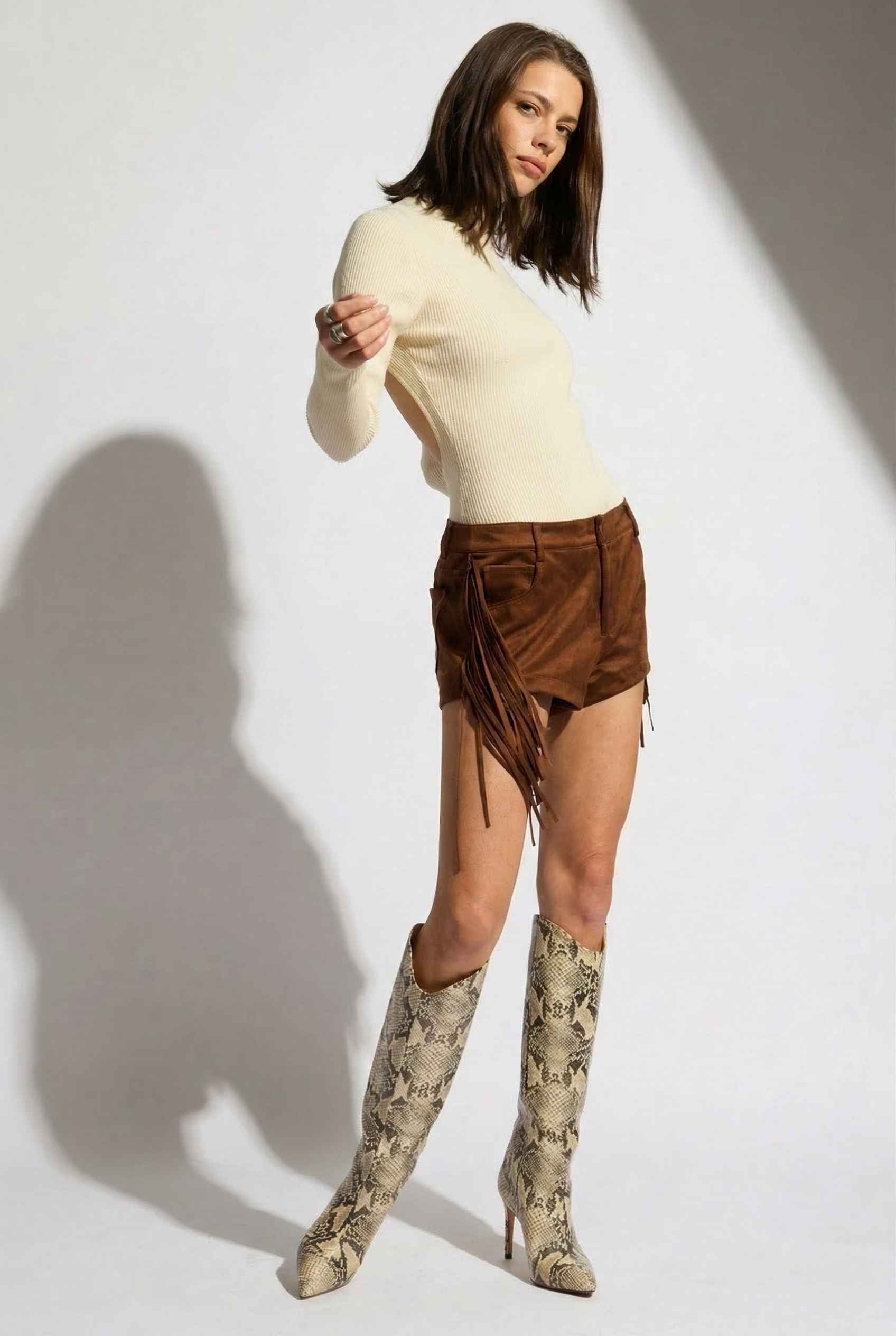 Model wearing Kiera Bodysuit Ribbed Knit Turtleneck Long Sleeve Bodysuit in Ivory with suede shorts and tall snake boots