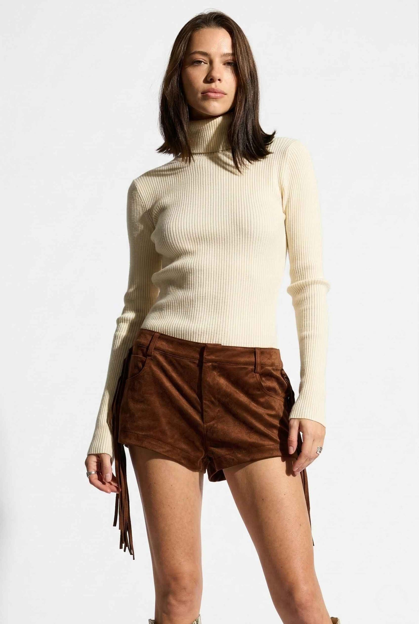Model wearing Kiera Bodysuit Ribbed Knit Turtleneck Long Sleeve Bodysuit in Ivory with suede shorts