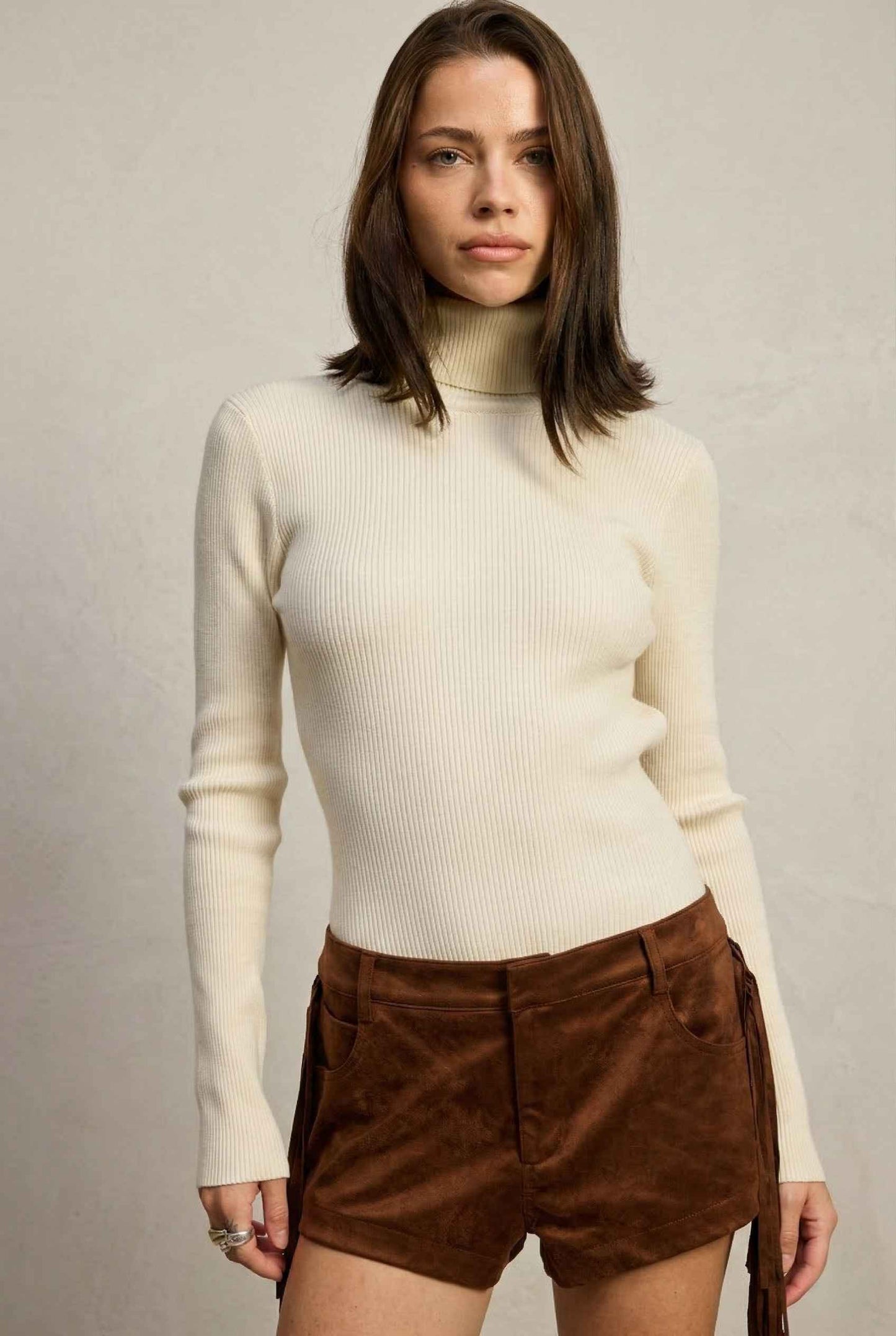 Model wearing Kiera Bodysuit Ribbed Knit Turtleneck Long Sleeve Bodysuit in Ivory with suede shorts