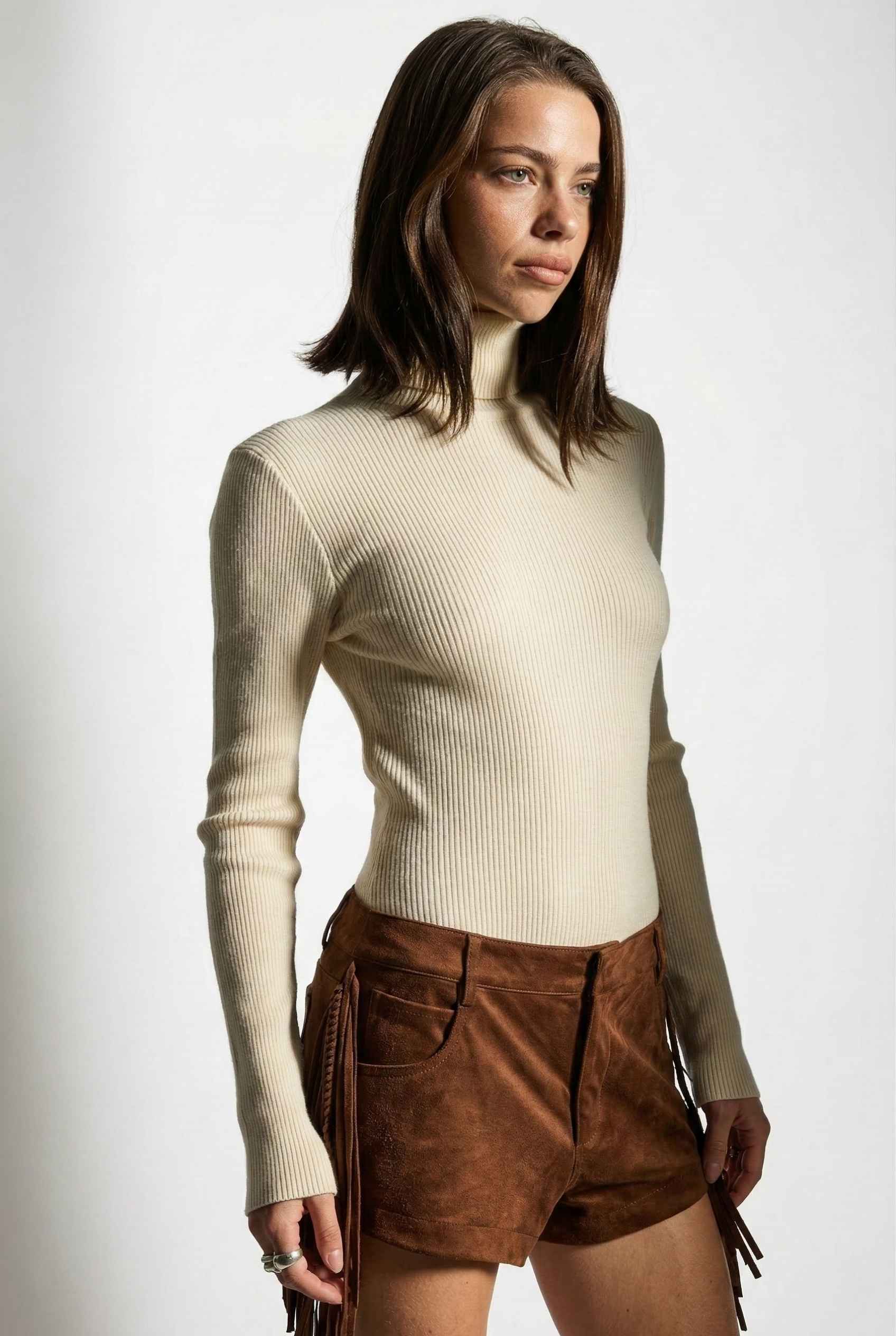 Model wearing Kiera Bodysuit Ribbed Knit Turtleneck Long Sleeve Bodysuit in Ivory with suede shorts