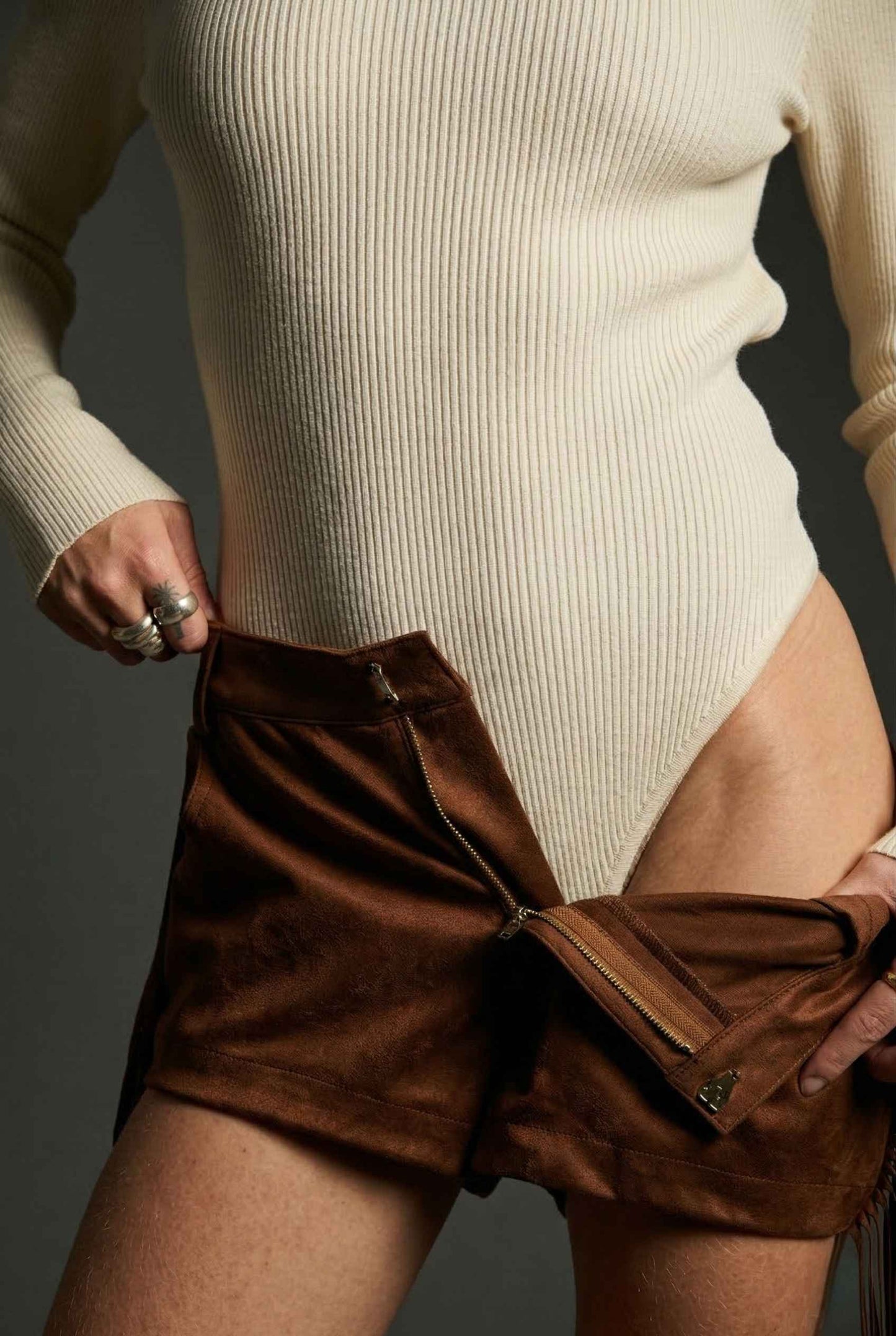 Model wearing Kiera Bodysuit Ribbed Knit Turtleneck Long Sleeve Bodysuit in Ivory with suede shorts