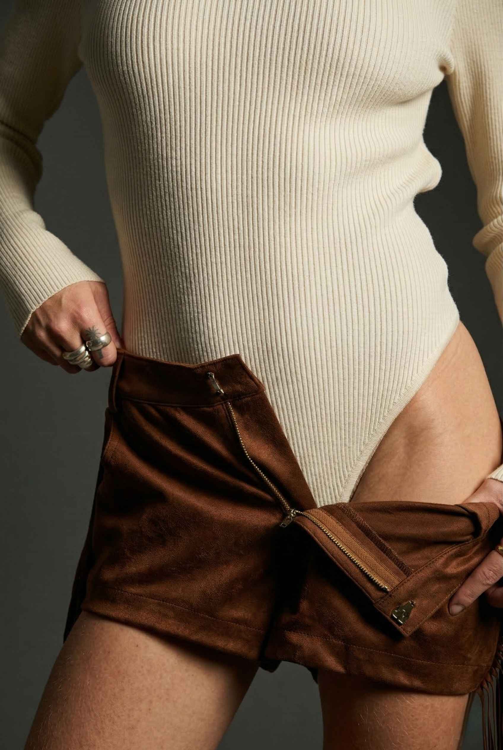 Model wearing Kiera Bodysuit Ribbed Knit Turtleneck Long Sleeve Bodysuit in Ivory with suede shorts