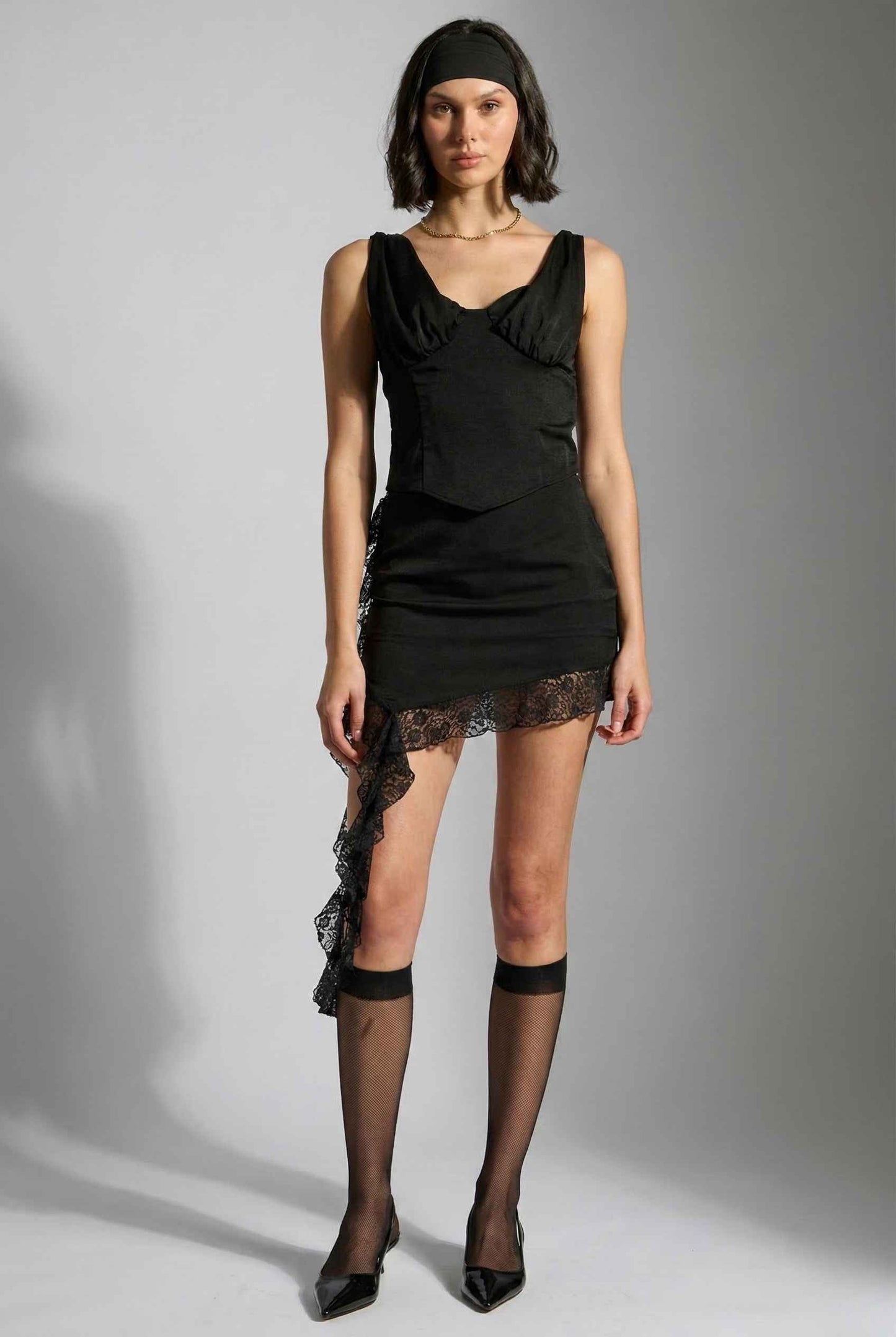 Woman wearing a Kiera Top Black Satin Cowl Neck Corset Tank with lace details on a gray background