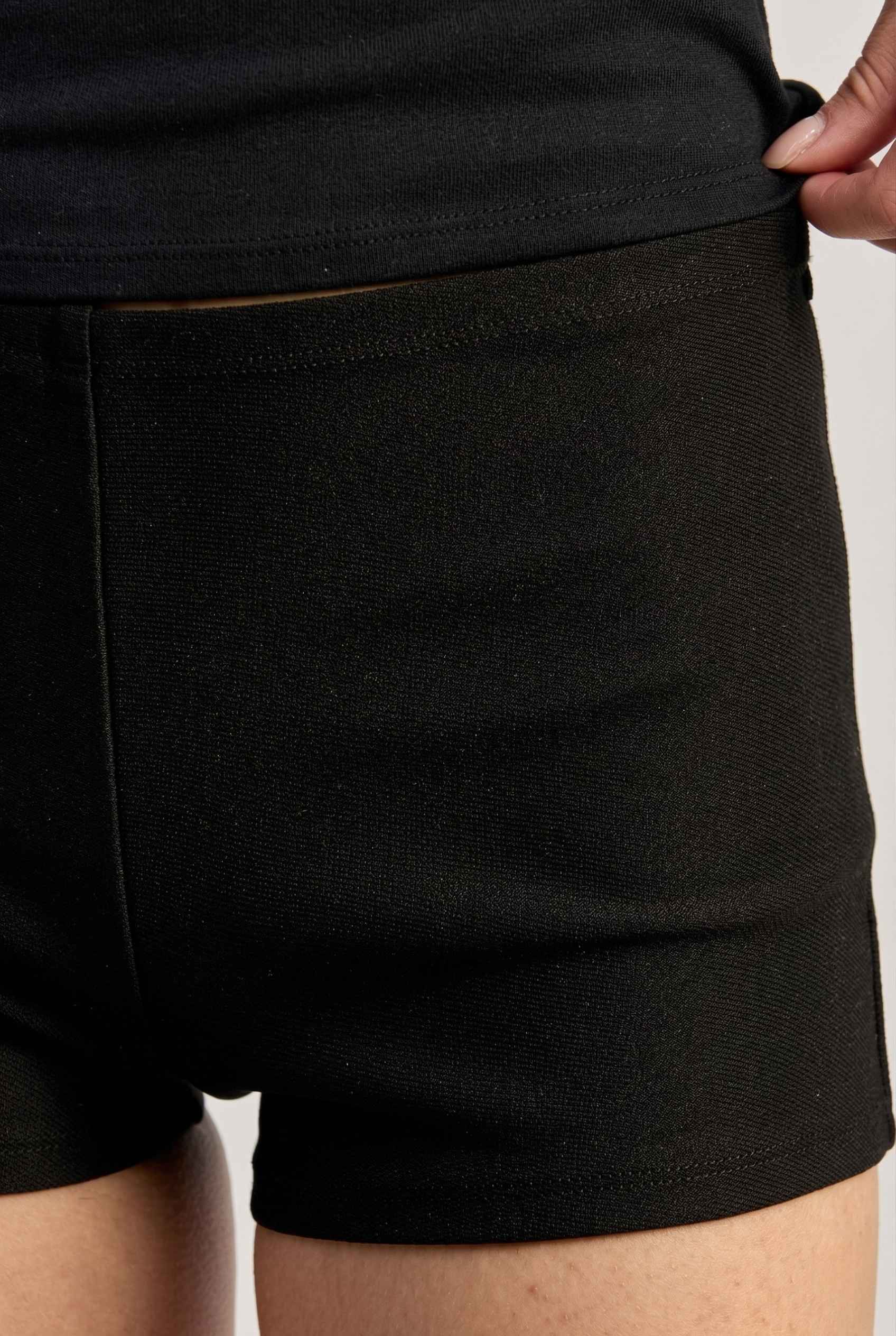 Kyra Shorts Black Rayon-Blend Knit Micro Biker Shorts being adjusted on a woman against a neutral background
