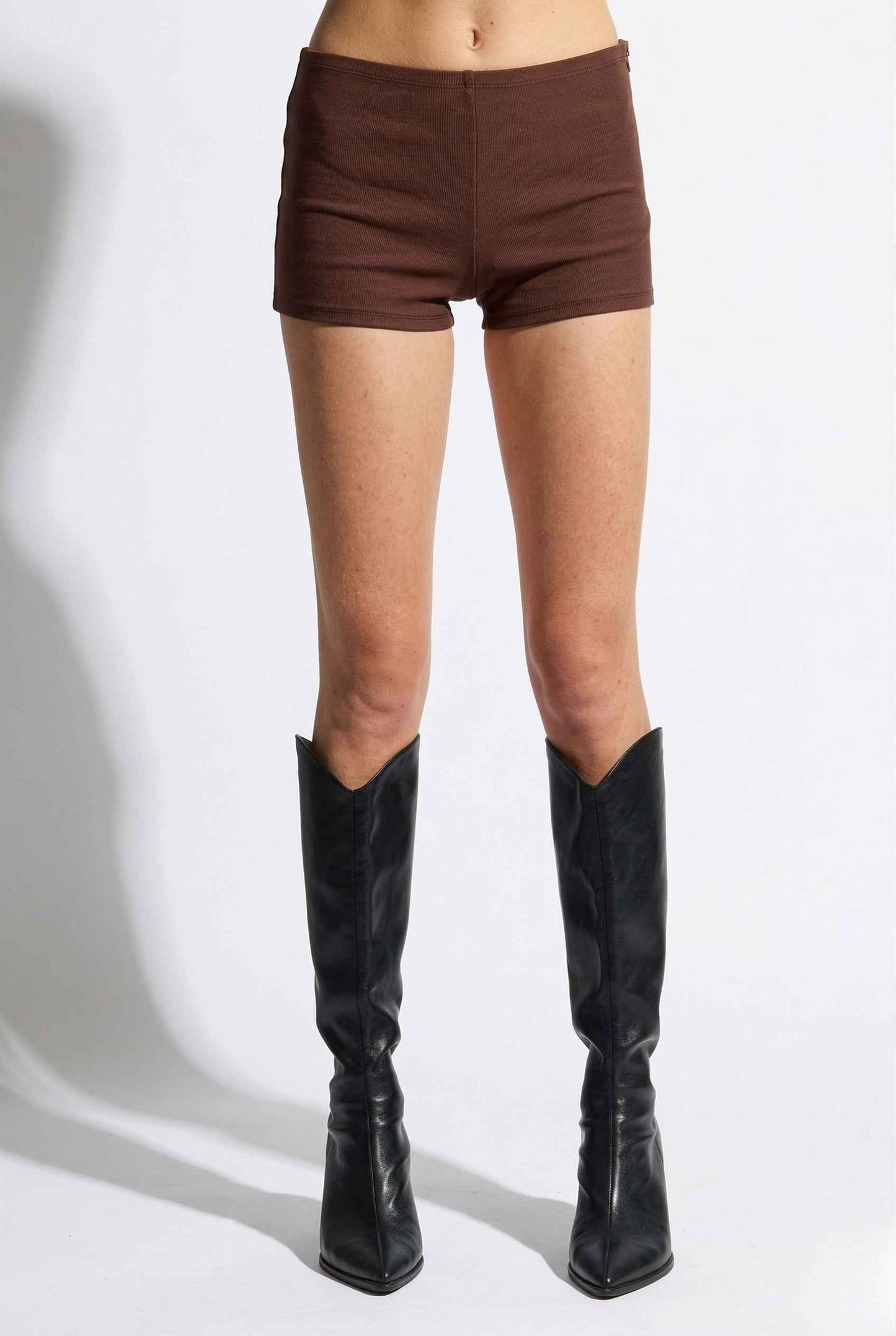 Woman wearing Kyra Shorts Brown Rayon-Blend Knit Micro Biker Shorts and knee-high boots on a white background