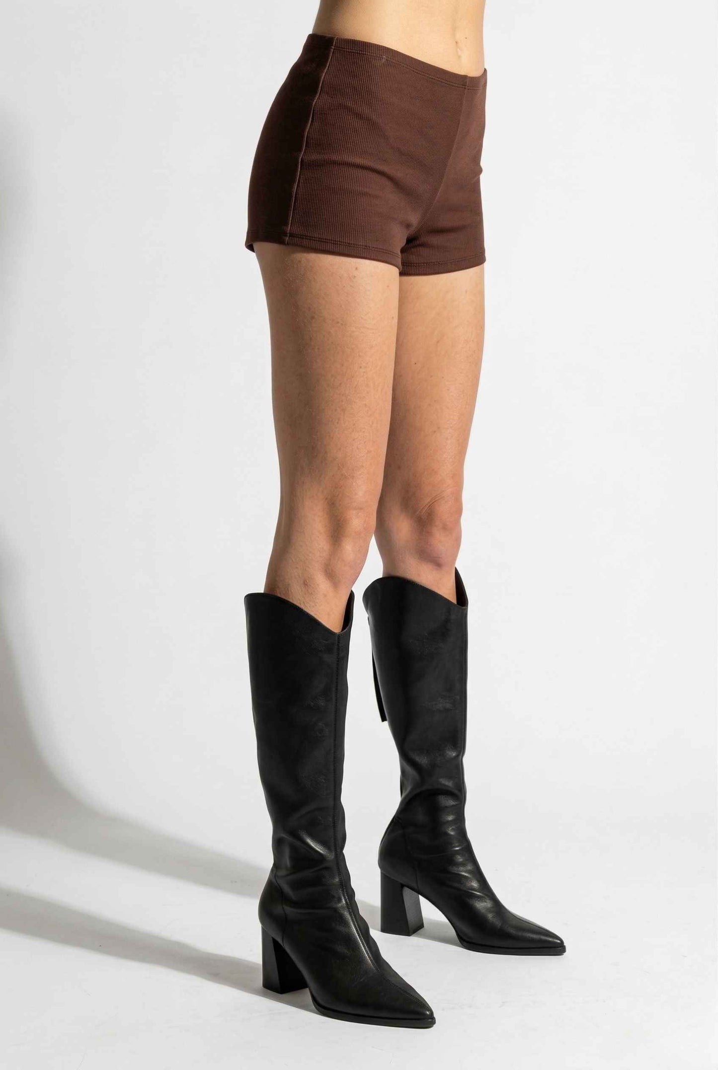Woman wearing Kyra Shorts Brown Rayon-Blend Knit Micro Biker Shorts and knee-high boots on a white background