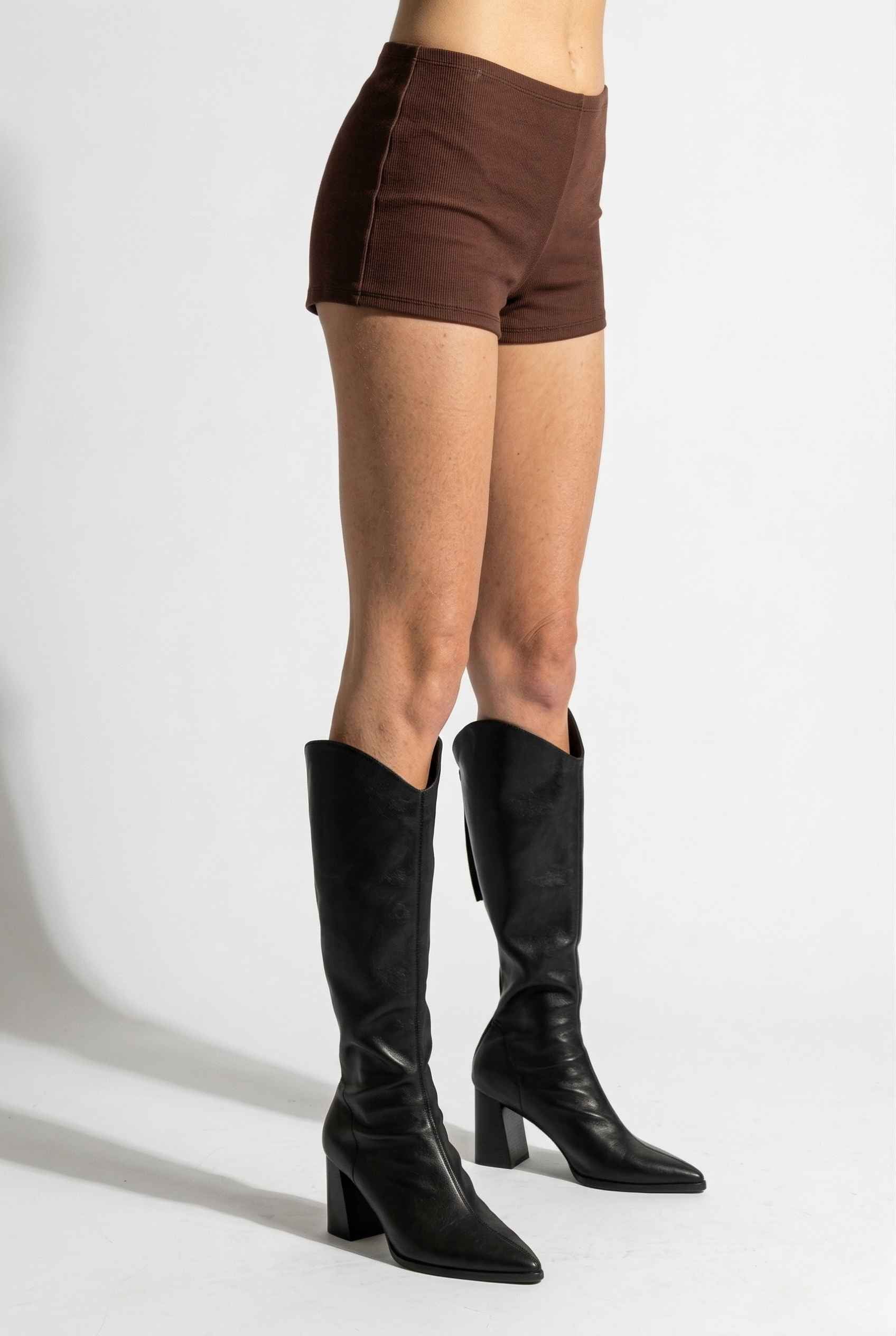 Woman wearing Kyra Shorts Brown Rayon-Blend Knit Micro Biker Shorts and knee-high boots on a white background