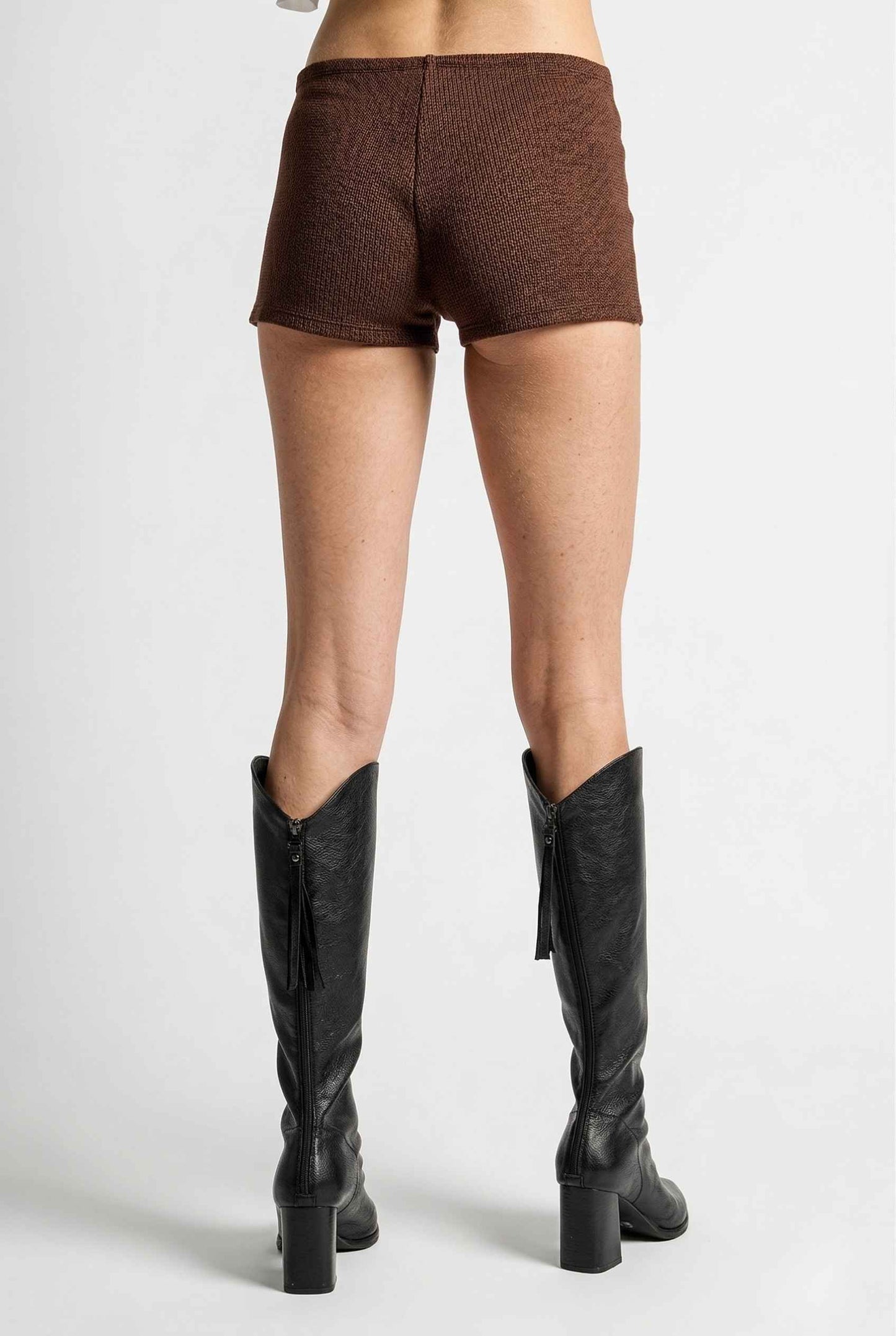 Woman wearing Kyra Shorts Brown Rayon-Blend Knit Micro Biker Shorts and knee-high boots on a white background