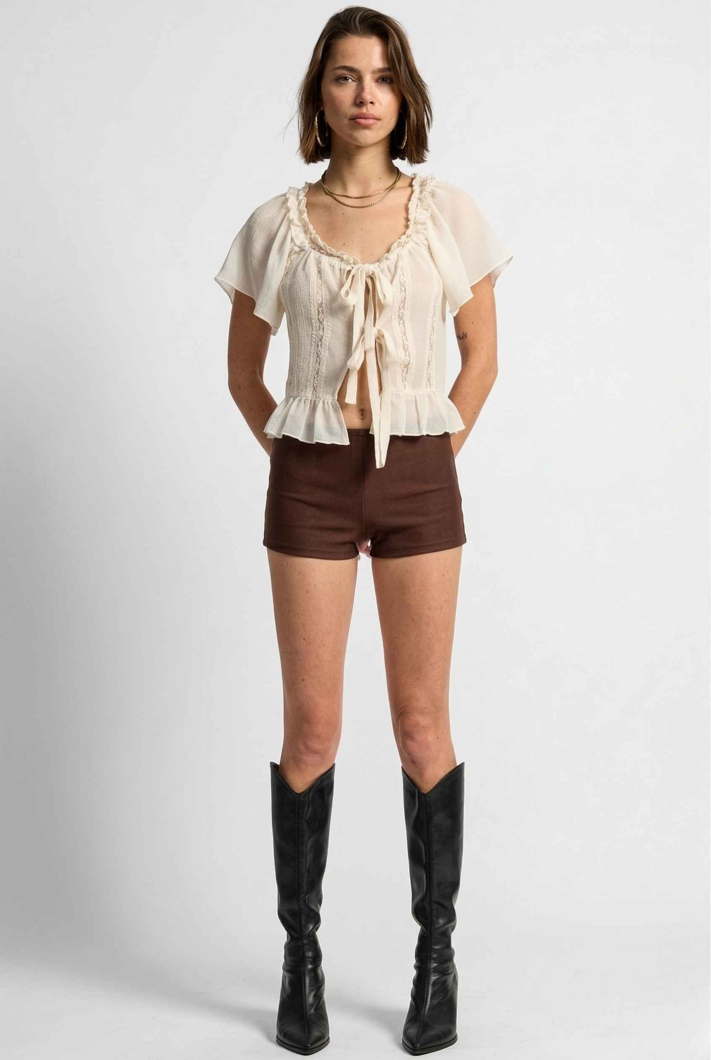 Woman wearing a beige top, Kyra Shorts Brown Rayon-Blend Knit Micro Biker Shorts, and knee-high boots on a white background