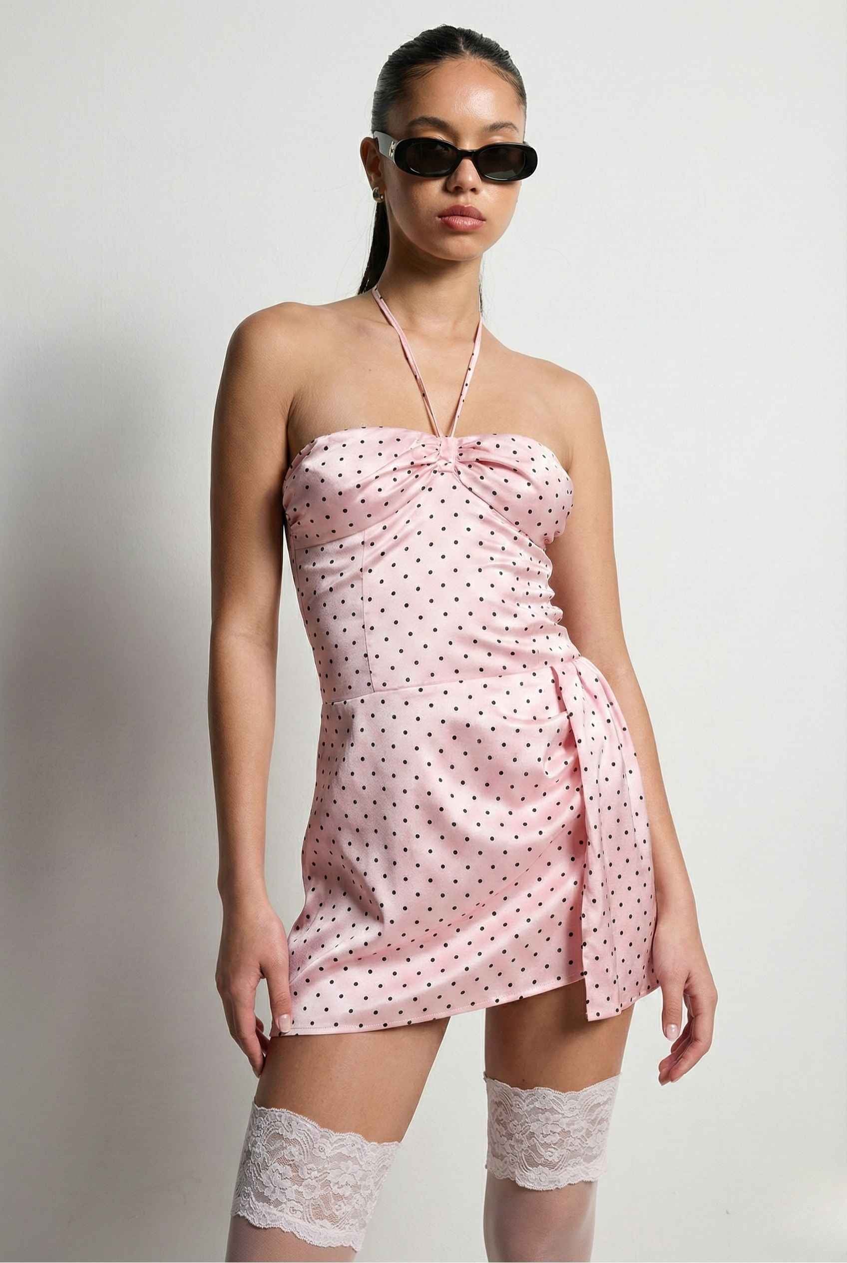 Woman wearing a Lola Mini Pink Polka Dot Satin Halter Dress with a plain background
