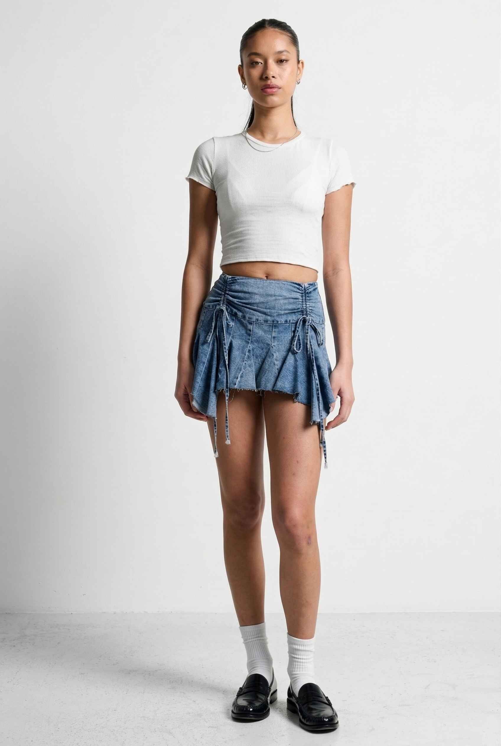 Model wearing Lola Skirt in light Blue Denim Ruched Waist Mini with Ruffle Hem with basic cropped t-shirt, socks and loafers