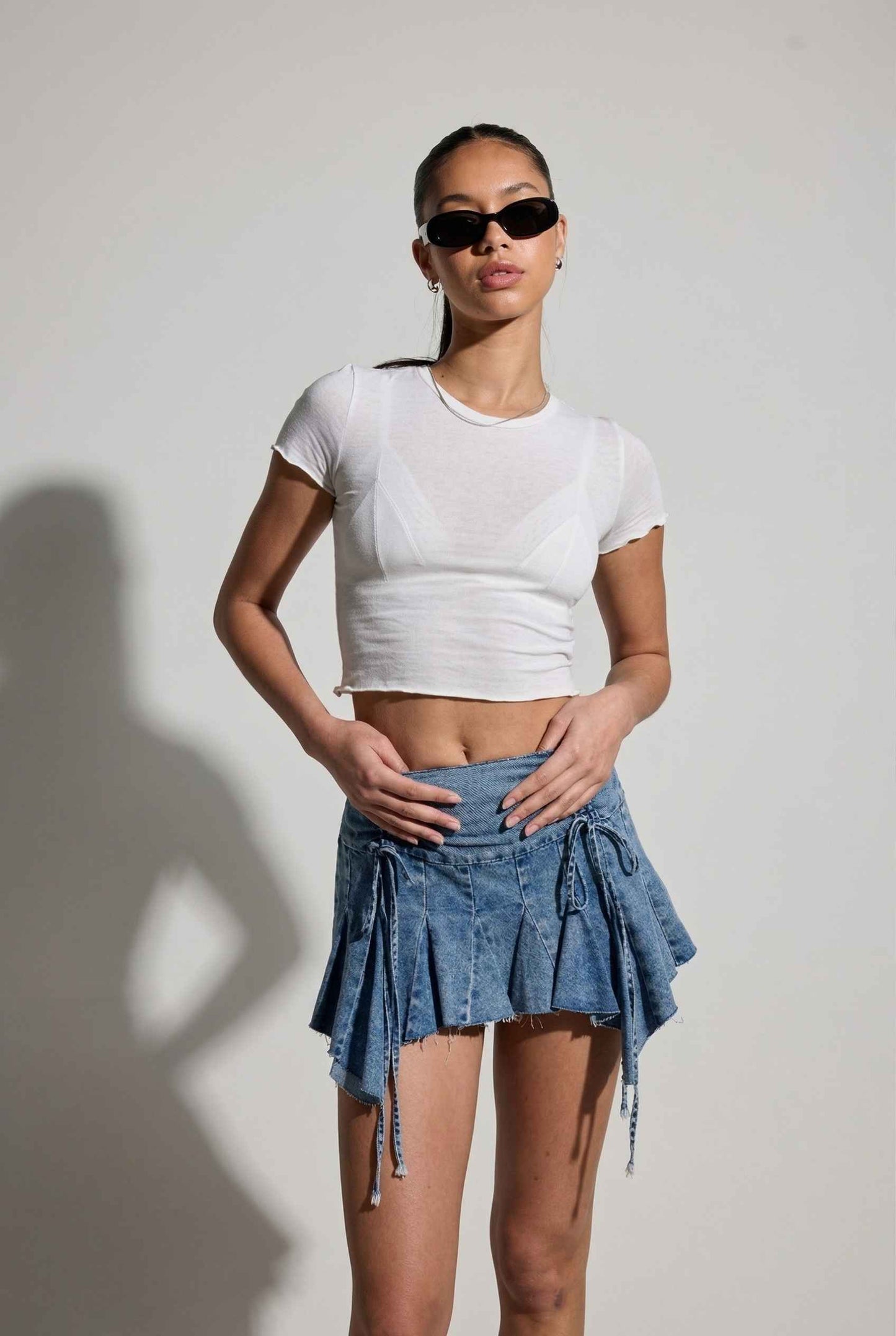Model wearing Lola Skirt in light Blue Denim Ruched Waist Mini with Ruffle Hem with basic cropped t-shirt