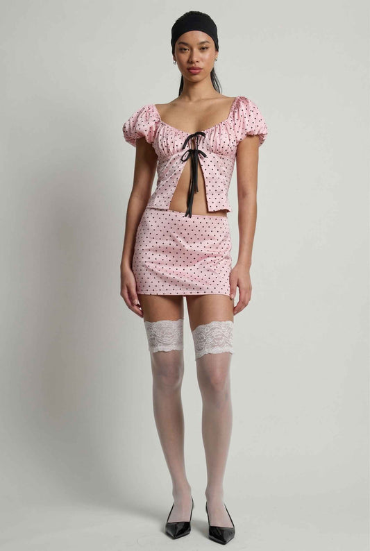 Model wearing Lola Skort in Pink Polka Dot Mini Skort with matching puff sleeve top paired with heels and lace stockings