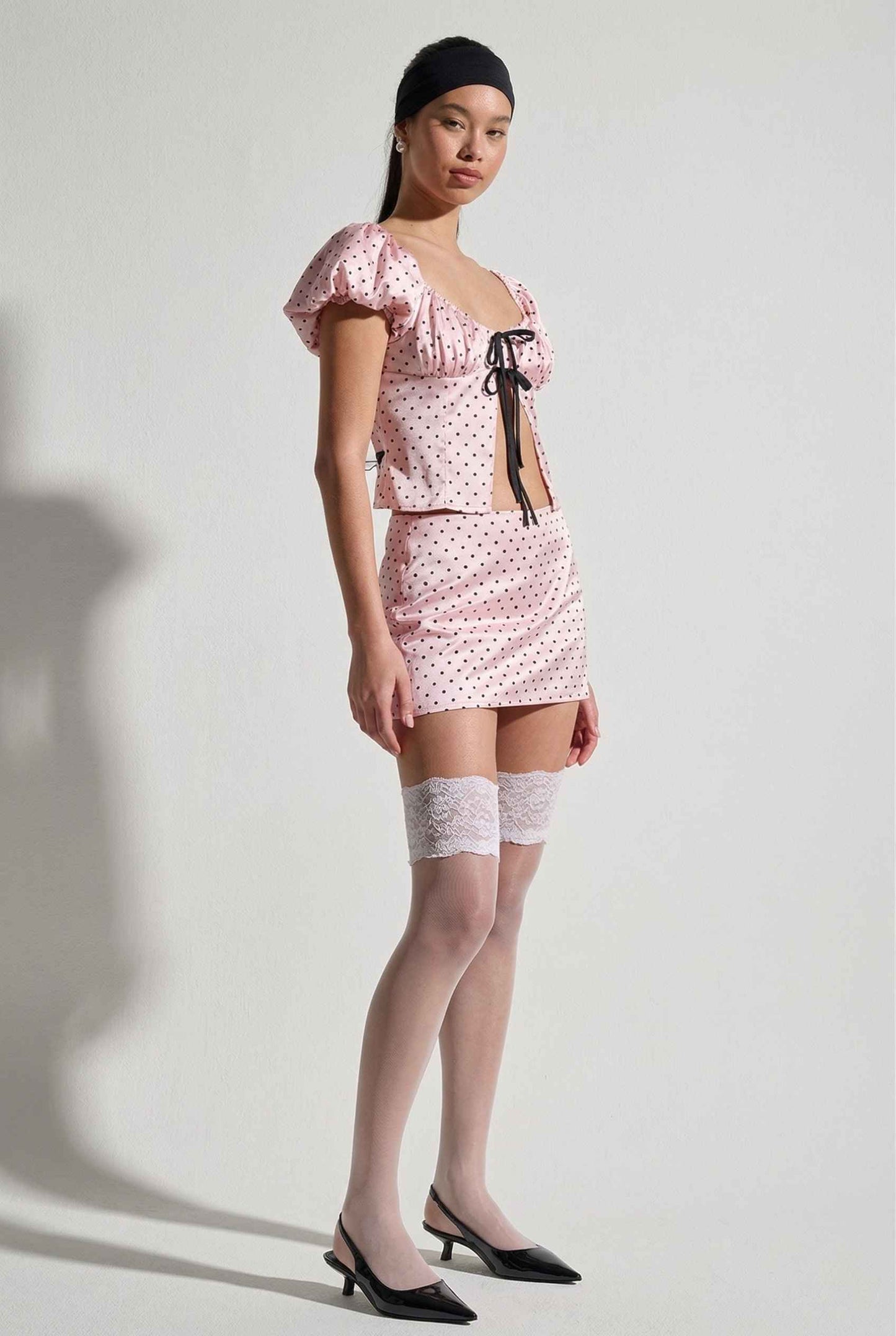 Model wearing Lola Skort in Pink Polka Dot Mini Skort with matching puff sleeve top paired with heels and lace stockings