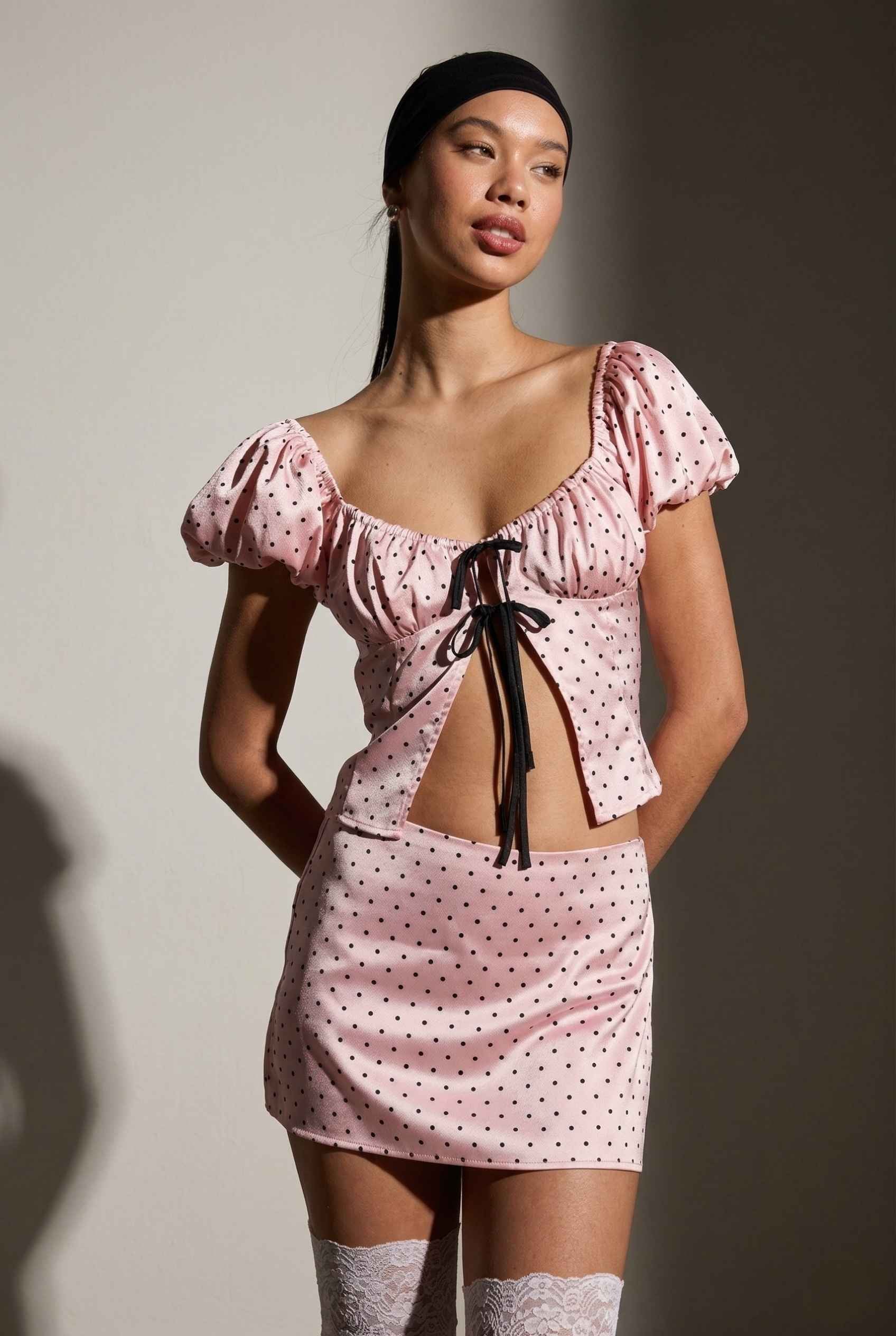 Model wearing Lola Skort in Pink Polka Dot Mini Skort with matching puff sleeve top paired with lace stockings