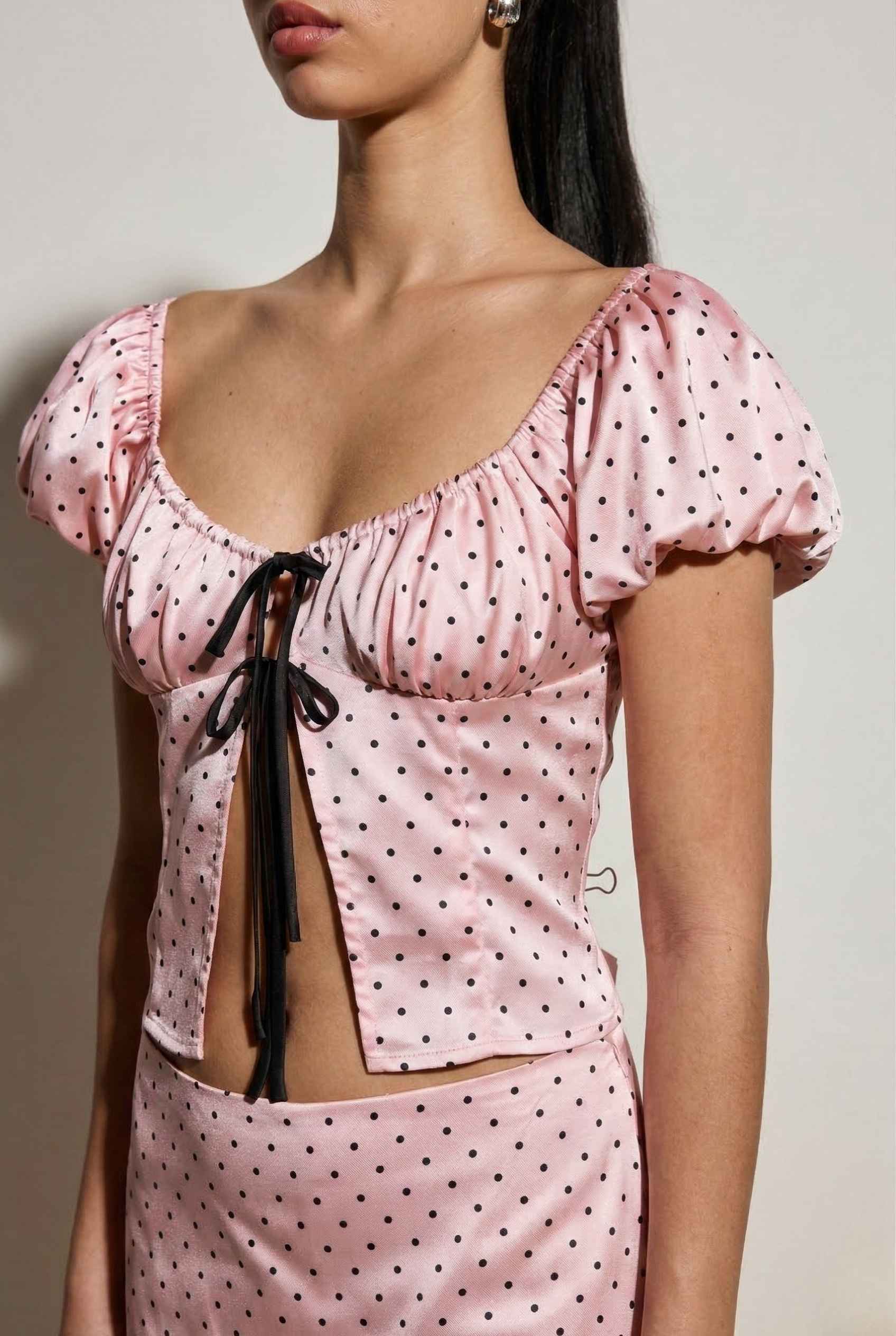 Woman wearing a Lola Top Pink & Black Polka Dot Puff Sleeve Tie-Front Blouse with puff sleeves against a neutral background