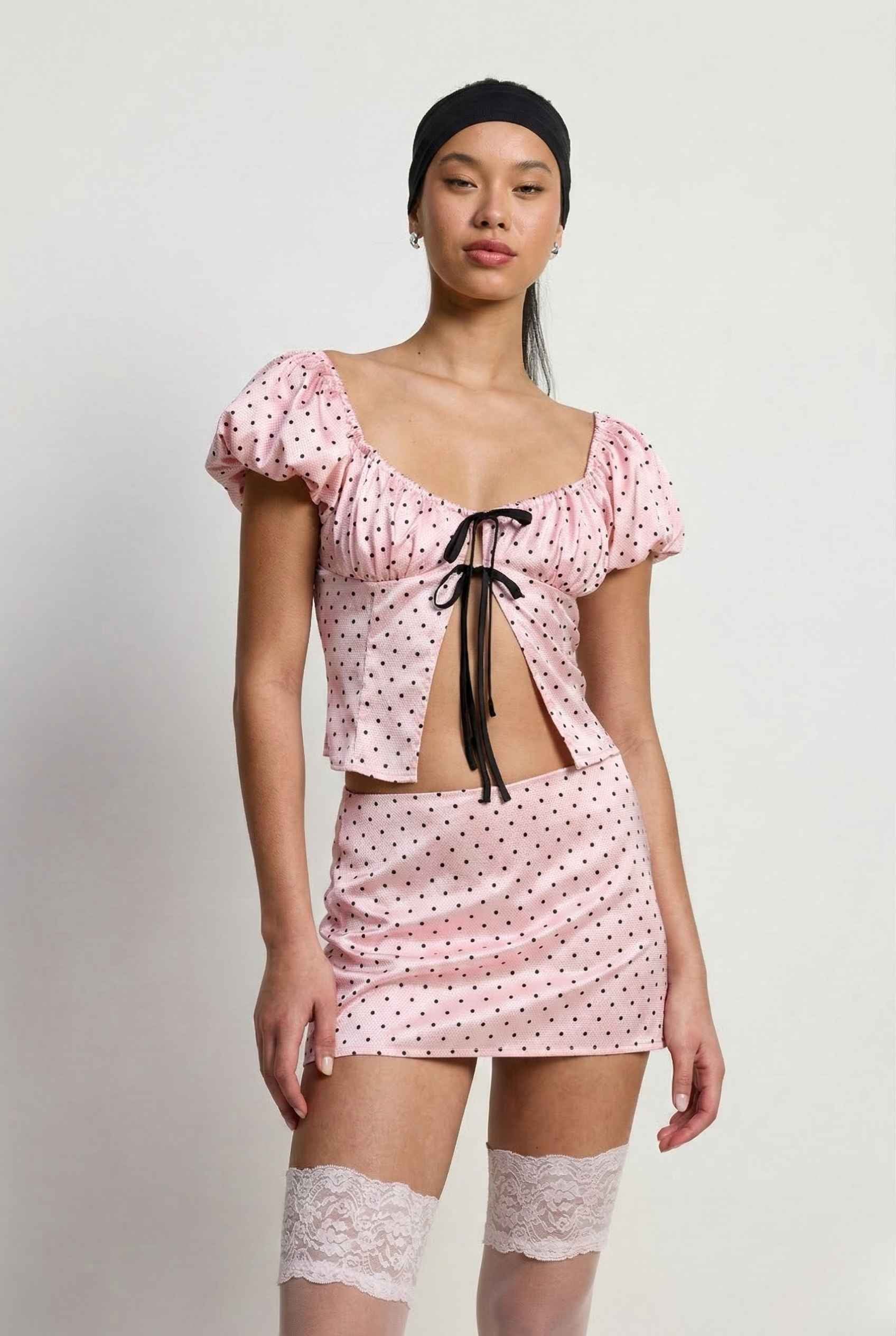 Woman wearing a Lola Top Pink & Black Polka Dot Puff Sleeve Tie-Front Blouse with a matching headscarf on a white background