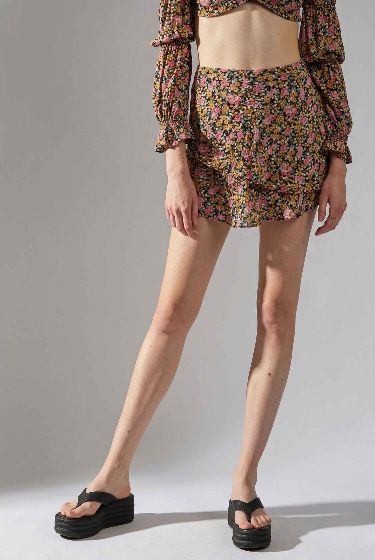 Woman wearing a Lyla Skort Black Ditsy Floral Linen-Blend Ruffle Mini Skort and a top on a plain background