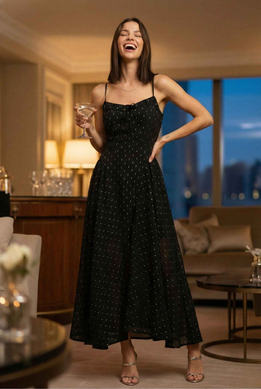 Woman in a Lyra Maxi Black Metallic Fleck Chiffon Dress holding a glass in a stylish room.