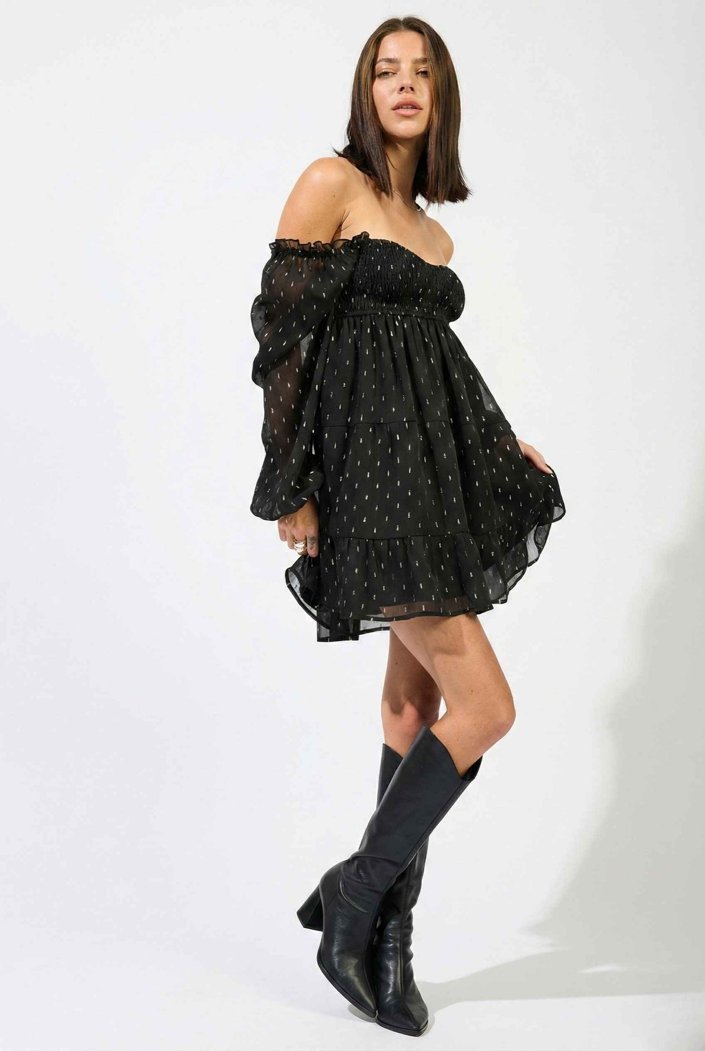 Woman wearing a Lyra Mini Black Smocked Long Sleeve Dress with sheer sleeves on a white background