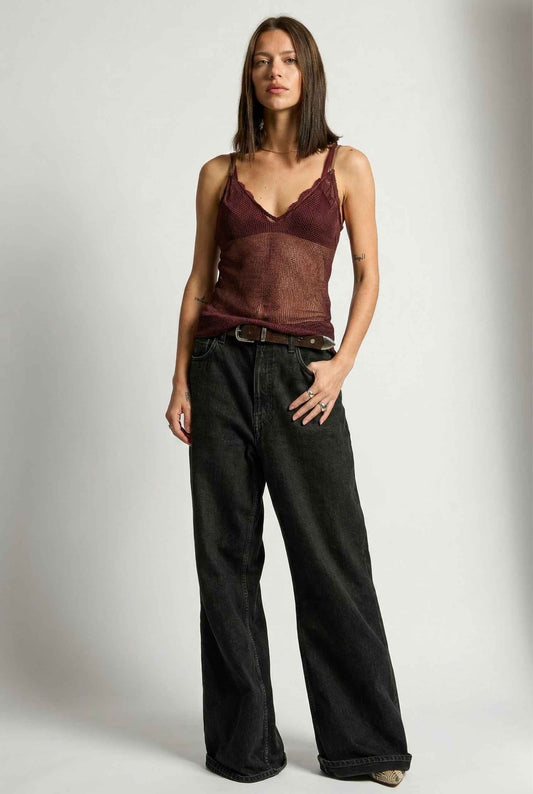 Woman wearing a Lyra Top Burgundy Metallic Chainmail Lace Trim Camisole and black wide-leg pants on a plain background