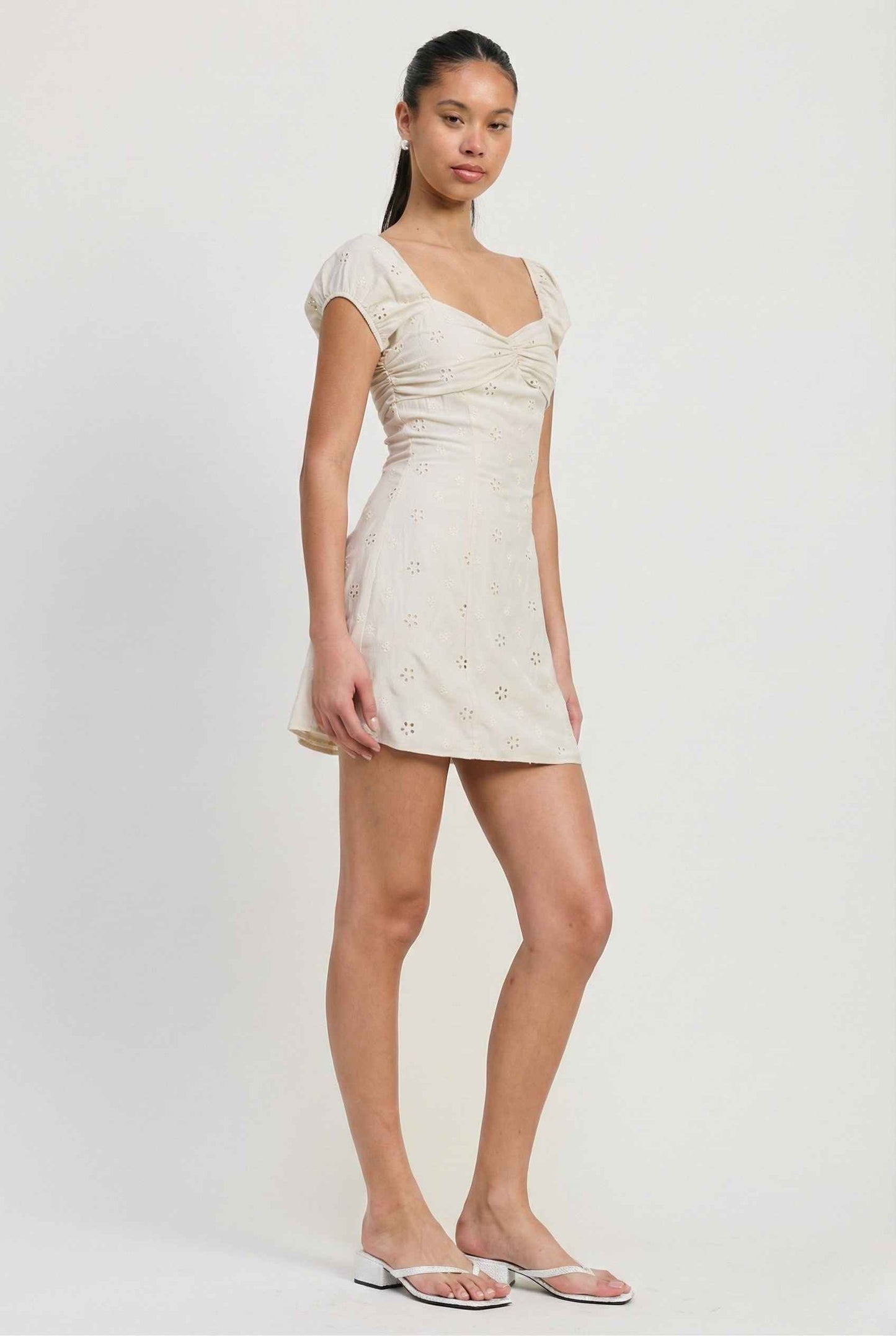 Woman wearing a Maeve Mini Ivory Eyelet Ruched Puff Sleeve Dress against a plain background