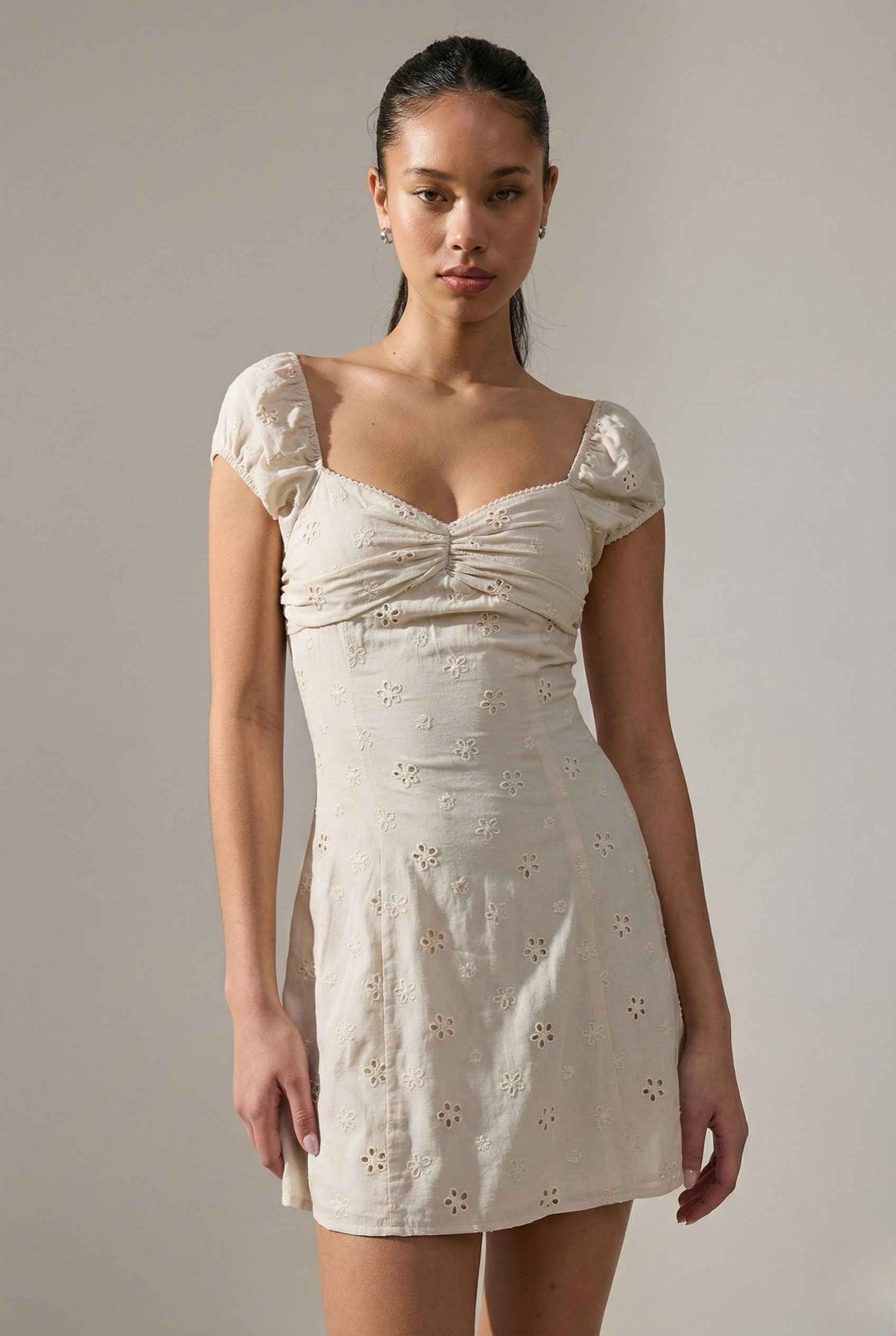 Woman wearing a Maeve Mini Ivory Eyelet Ruched Puff Sleeve Dress with floral details against a plain background