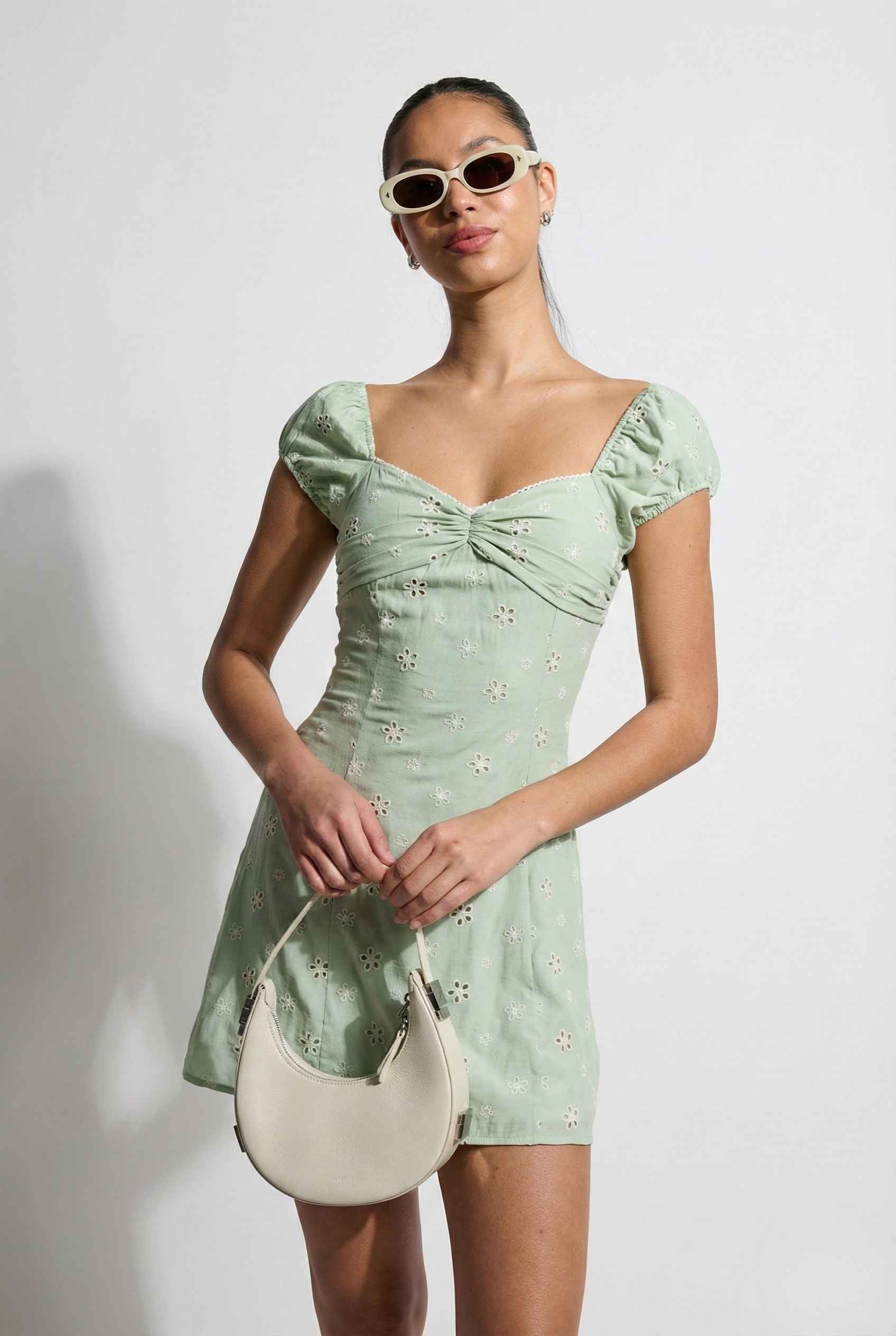 Woman wearing a Maeve Mini Mint Eyelet Ruched Puff Sleeve Dress with puffed sleeves and a white handbag against a plain background
