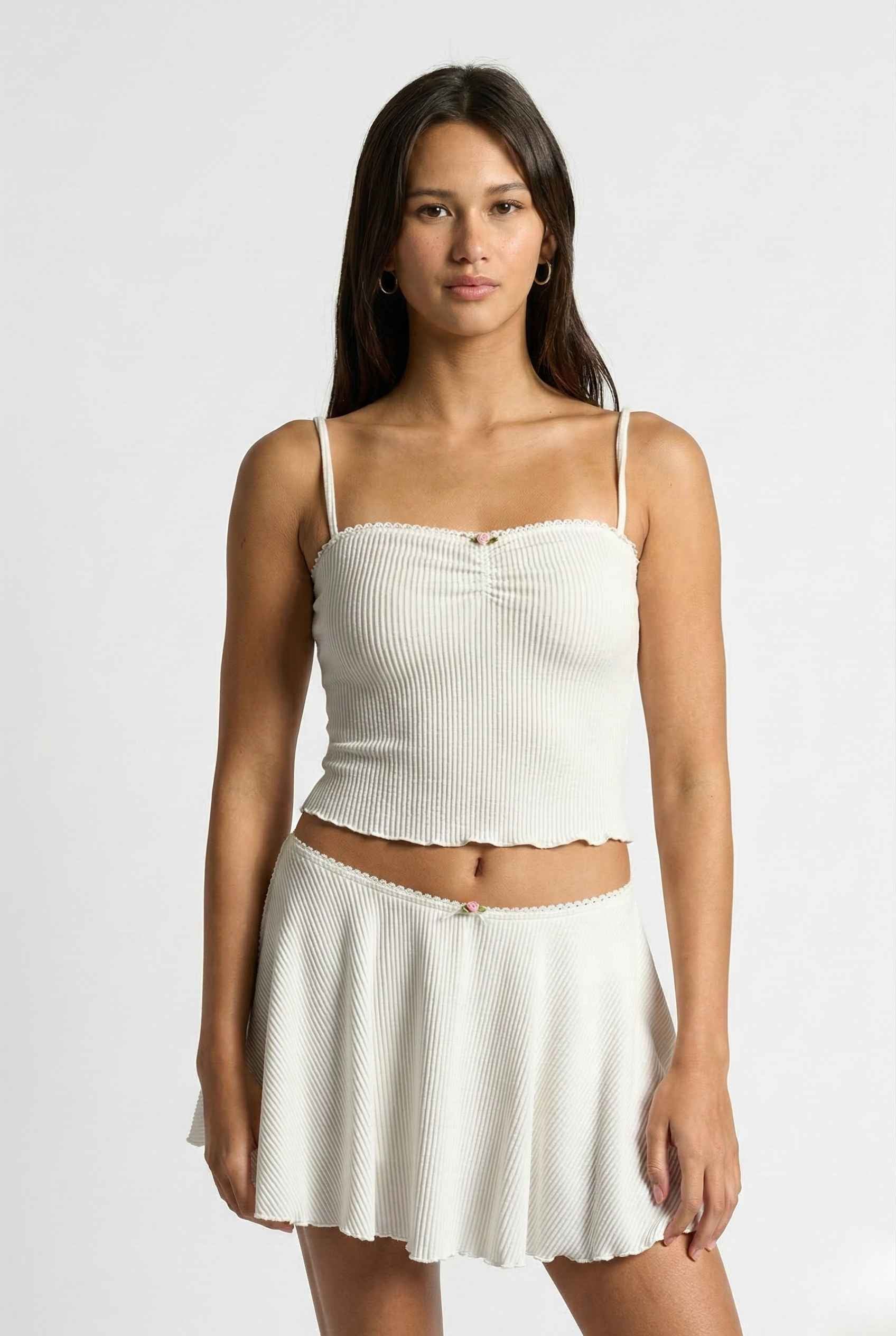 Woman wearing a Maisie Cami White Ribbed Knit Bow Top with Picot Trim and skirt set on a plain background