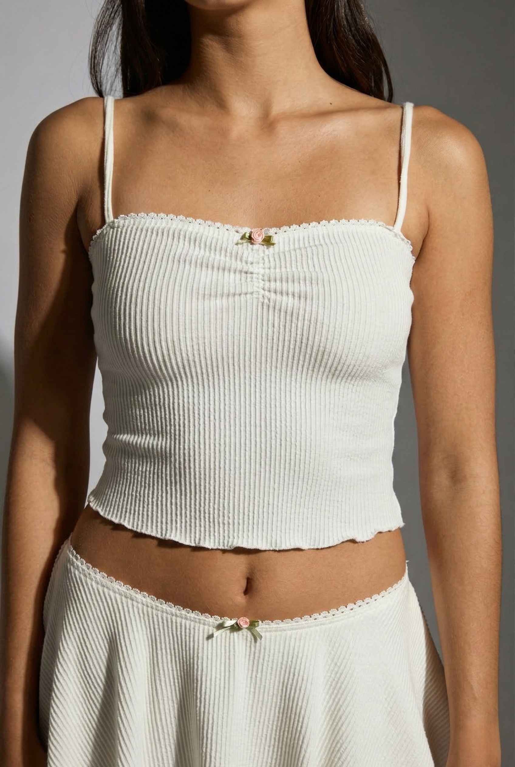 Woman wearing a Maisie Cami White Ribbed Knit Bow Top with Picot Trim and skirt set against a neutral background