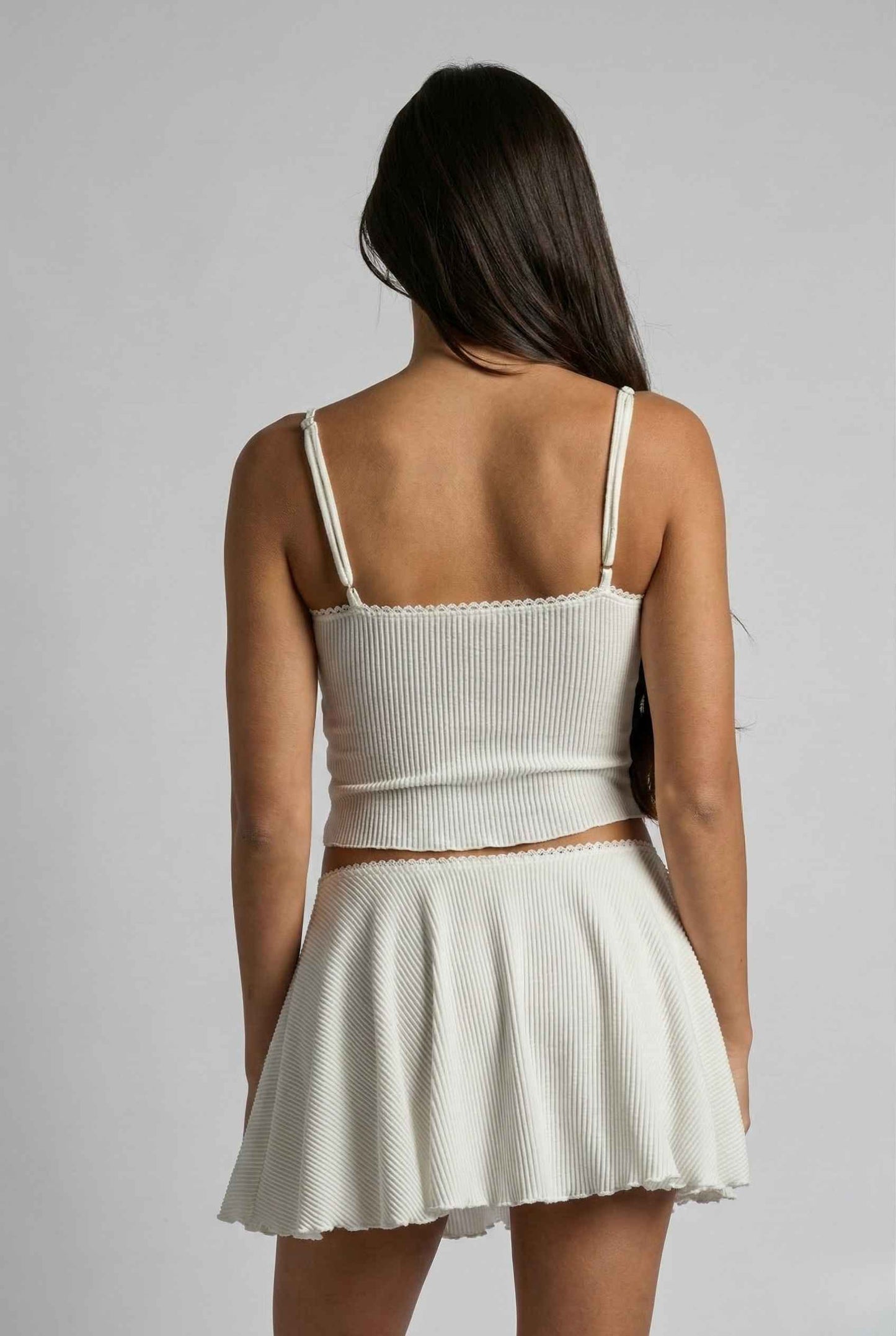 Woman wearing a Maisie Cami White Ribbed Knit Bow Top with Picot Trim against a gray background