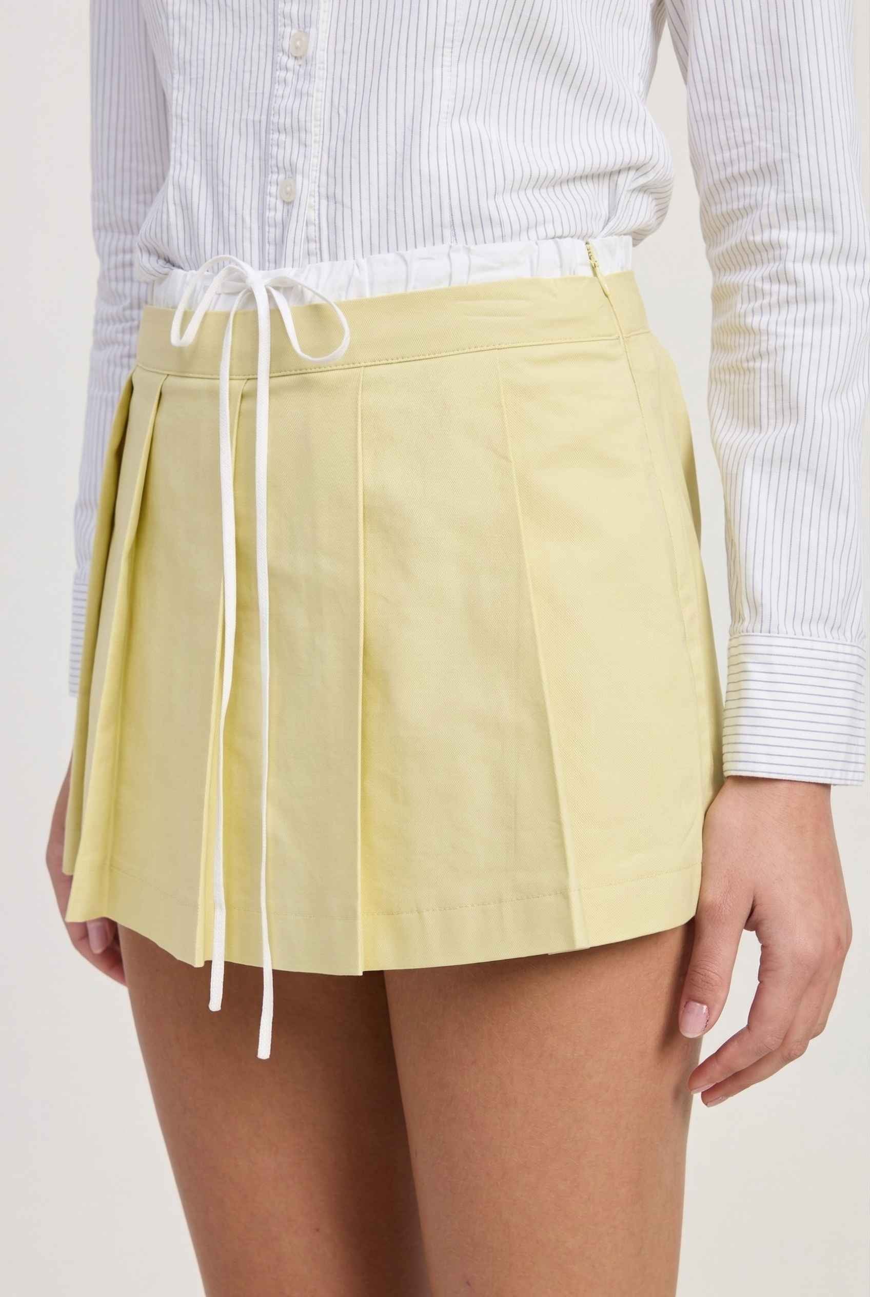 Model wearing Margo Skort in Yellow Poplin Cotton Twill Pleated Mini Skort paired with crisp poplin blouse close up details