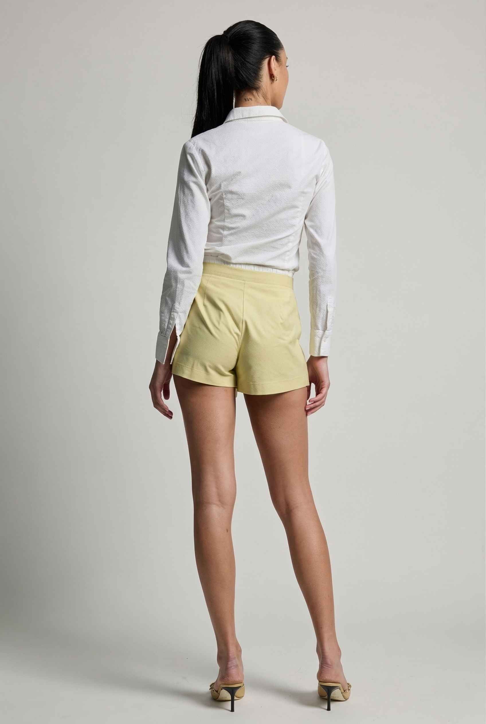 Model wearing Margo Skort in Yellow Poplin Cotton Twill Pleated Mini Skort paired with crisp poplin blouse and basic heels
