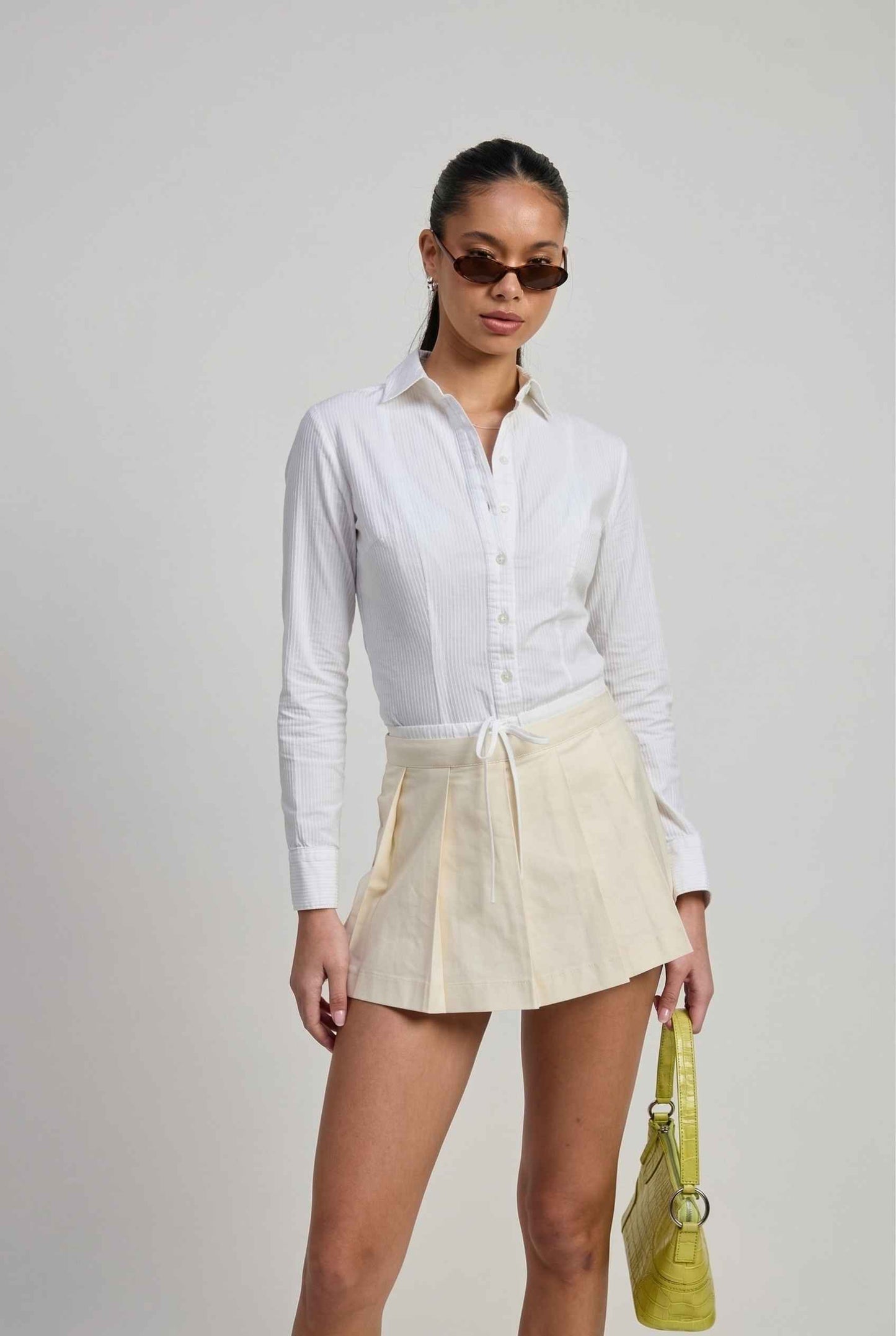 Model wearing Margo Skort in Ivory Poplin Cotton Twill Pleated Mini Skort paired with crisp poplin blouse and handbag