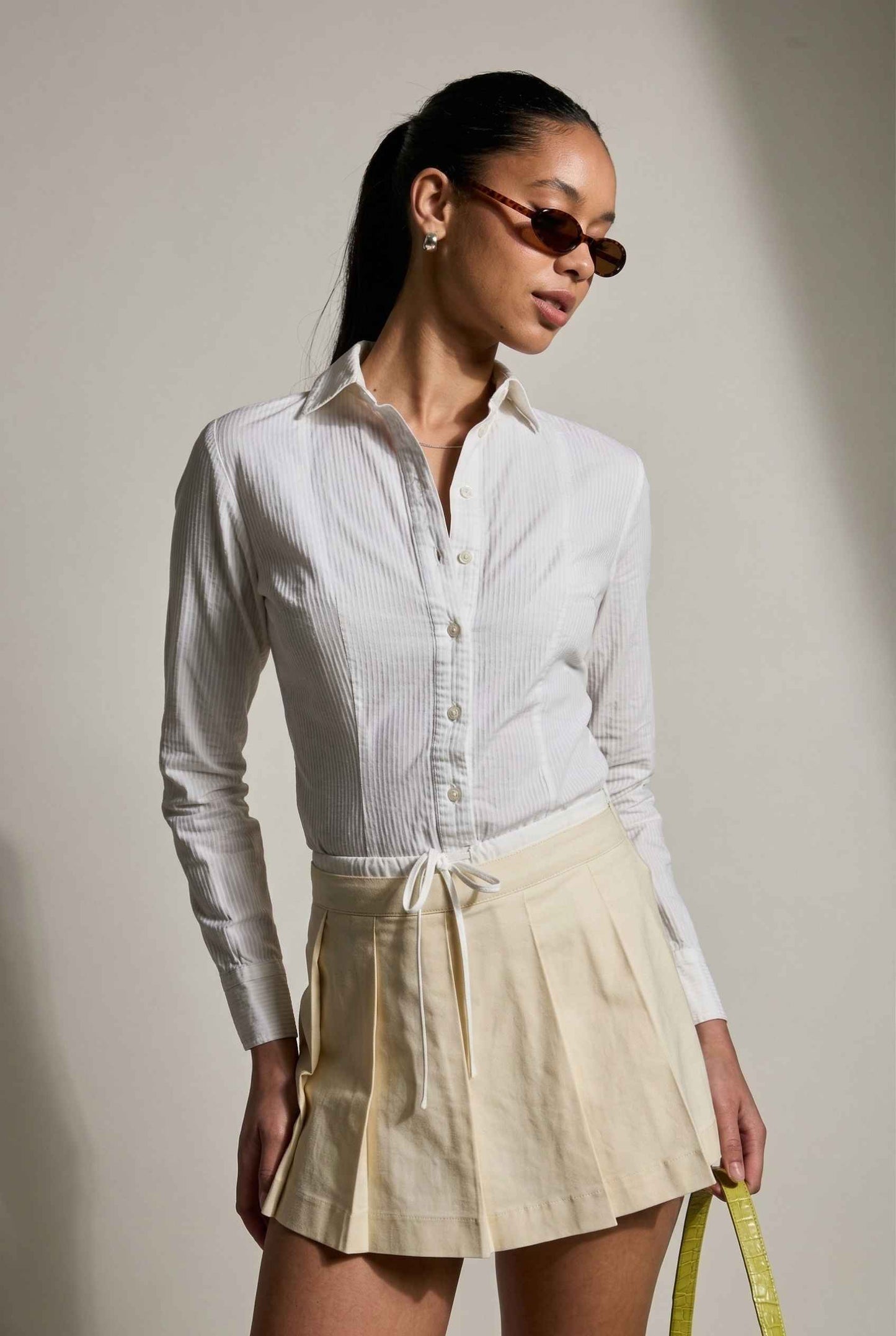Model wearing Margo Skort in Ivory Poplin Cotton Twill Pleated Mini Skort paired with crisp poplin blouse and handbag