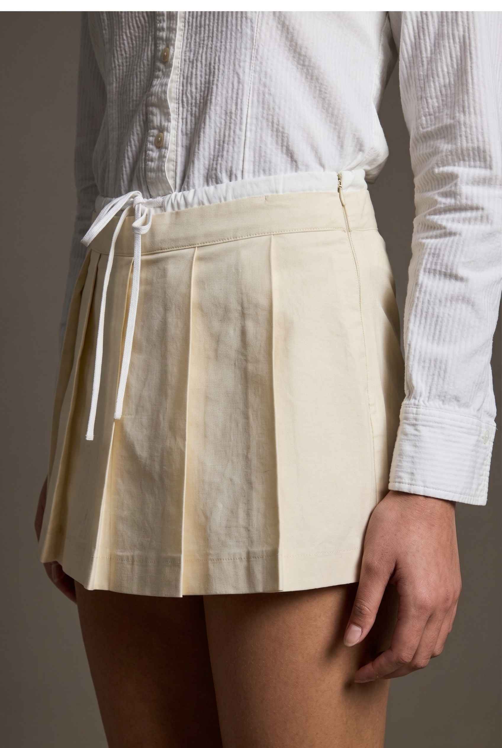 Model wearing Margo Skort in Ivory Poplin Cotton Twill Pleated Mini Skort paired with crisp poplin blouse tucked in