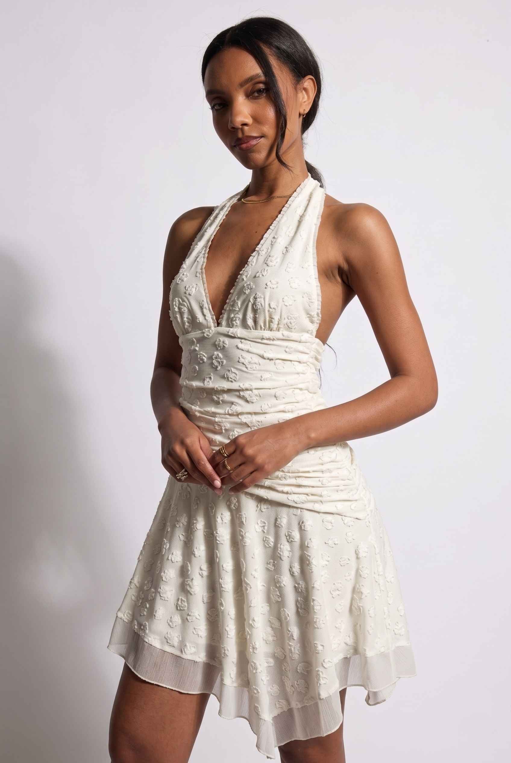Model wearing Mikala Ruched Halter Mini Dress in Ivory Cocktail Dress close up halter neckline and asymmetrical hem