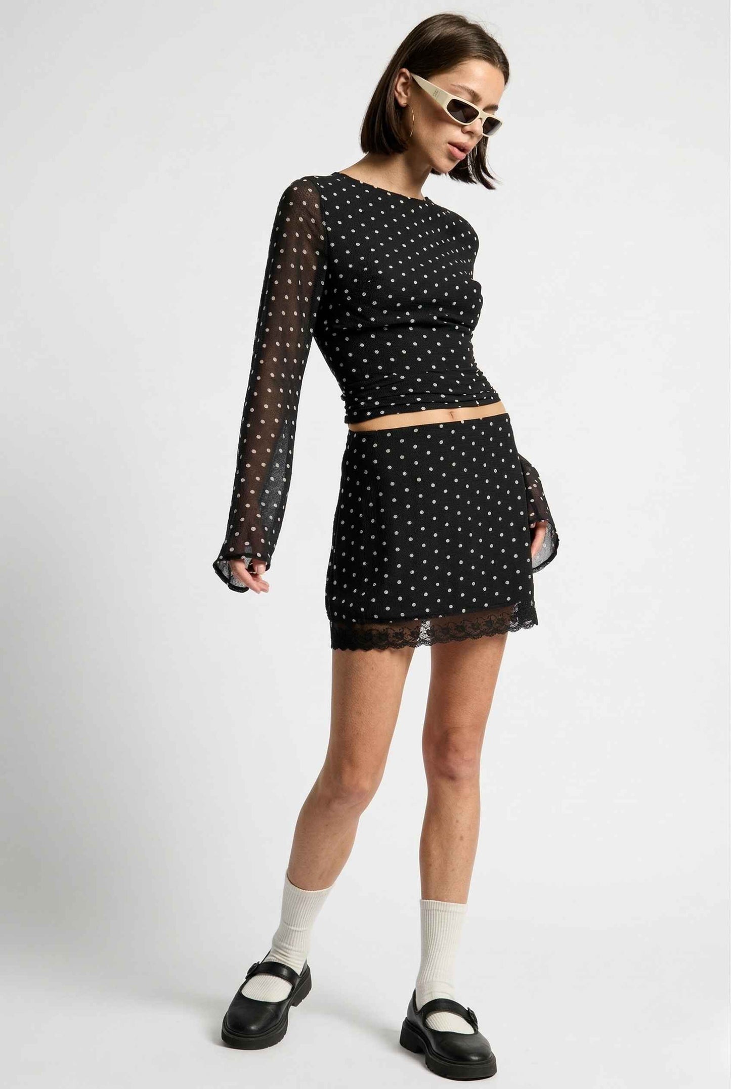 Woman wearing a Mila Skirt Black Polka Dot Mesh Mini Skirt with Lace Trim with sheer sleeves on a white background