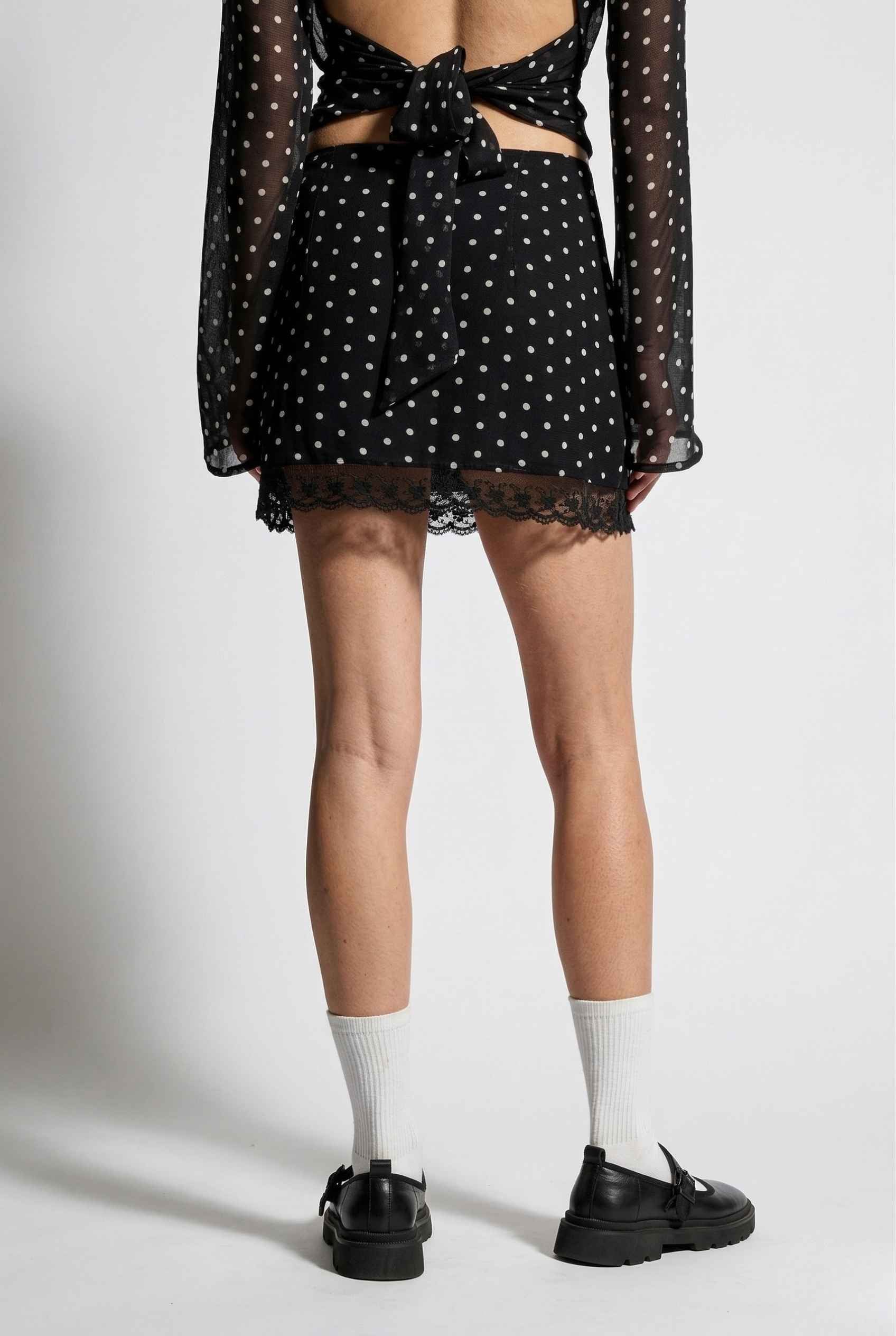 Woman wearing a Mila Skirt Black Polka Dot Mesh Mini Skirt with Lace Trim with cut-out design on a white background