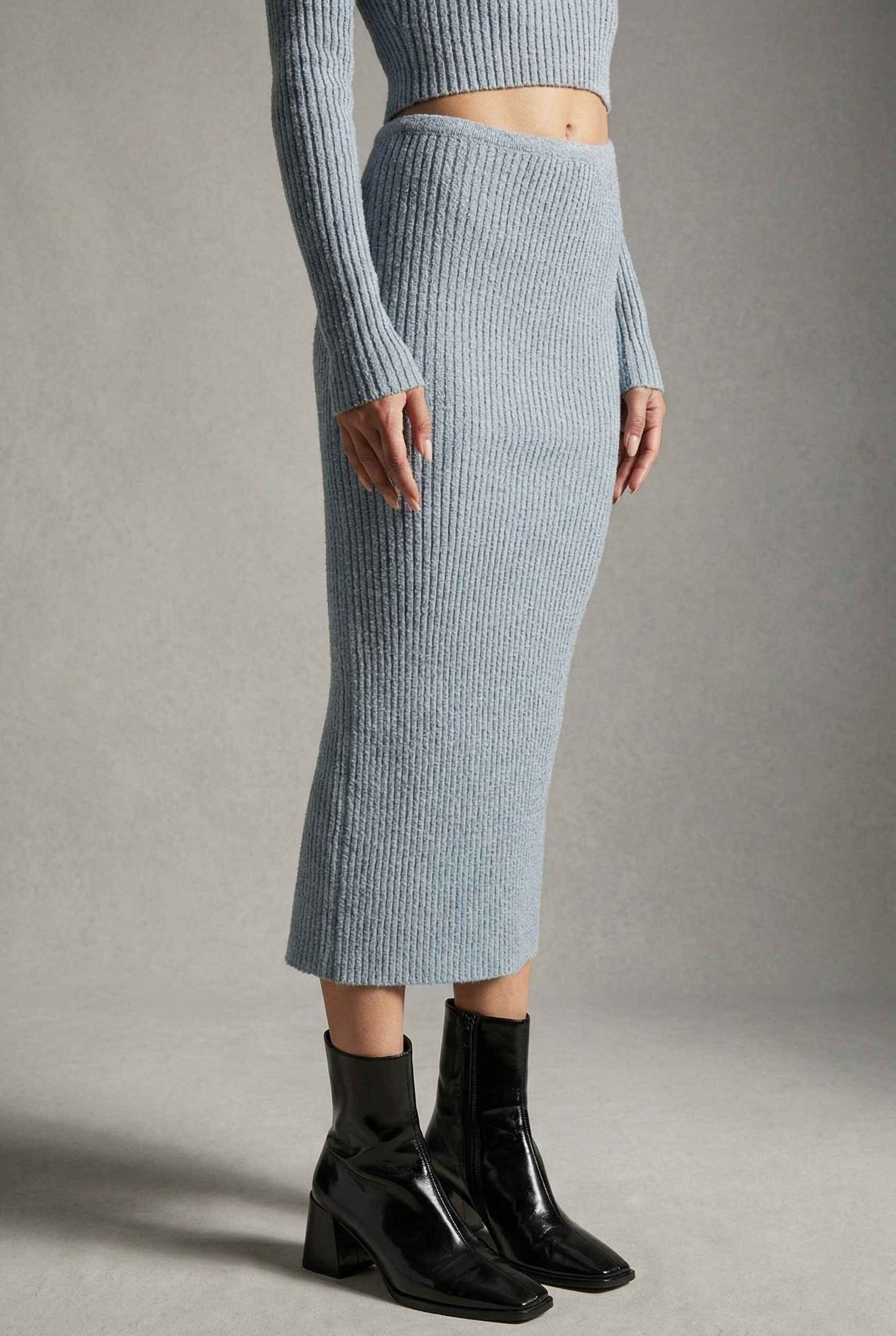 Model wearing Mila Skirt Marled Ribbed Knit Column Maxi Skirt in Light Blue with matching sweater top and heeled boots on a plain background