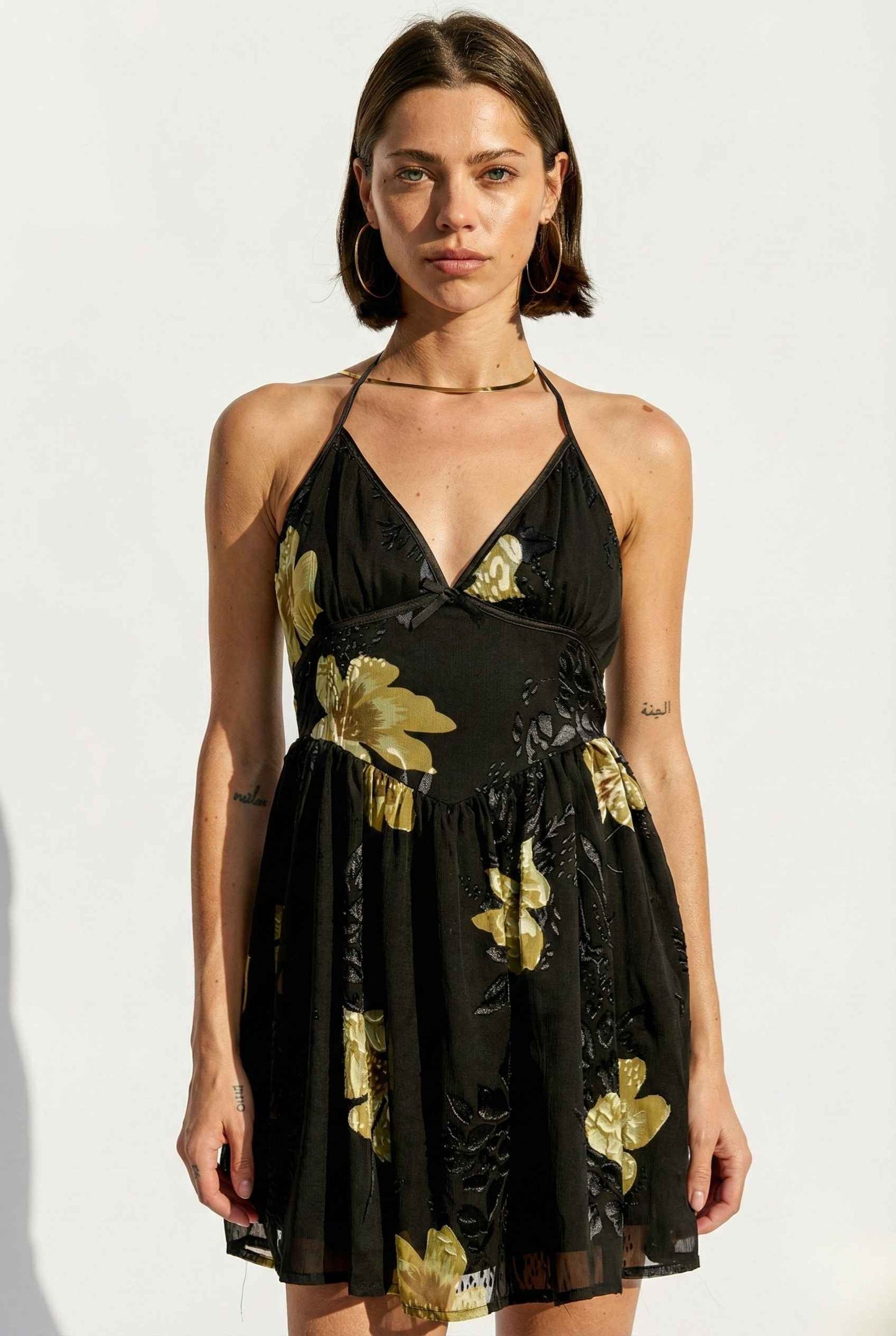 Woman wearing a Nina Mini Black & Gold Floral Halter Dress against a white background