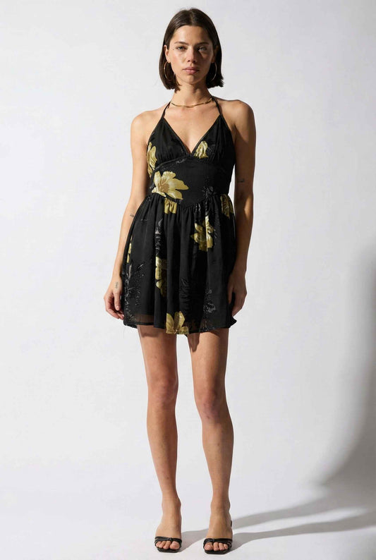 Woman wearing a Nina Mini Black & Gold Floral Halter Dress against a white background