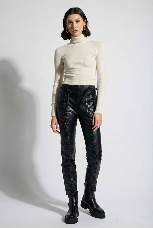 Model wearing Nova Pants in Black Vegan Leather High-Waist Lace-Up Trousers with ribbed sweater top and boots on plain background