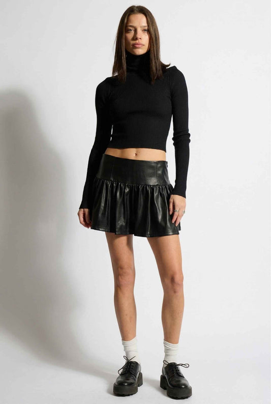 Woman wearing a black turtleneck and Nova Skirt Black Faux Leather Drop-Waist Ruffle Mini Skirt on a white background