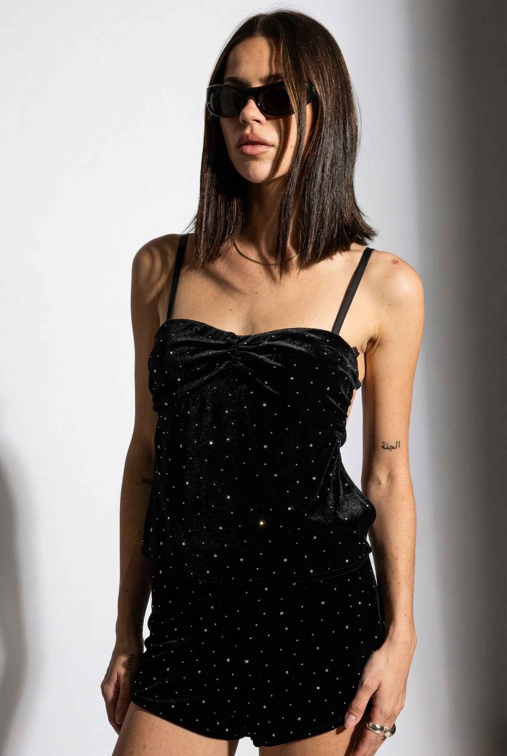 Woman wearing a Nova Top Black Velvet Rhinestone Ruched Camisole with thin straps against a plain background
