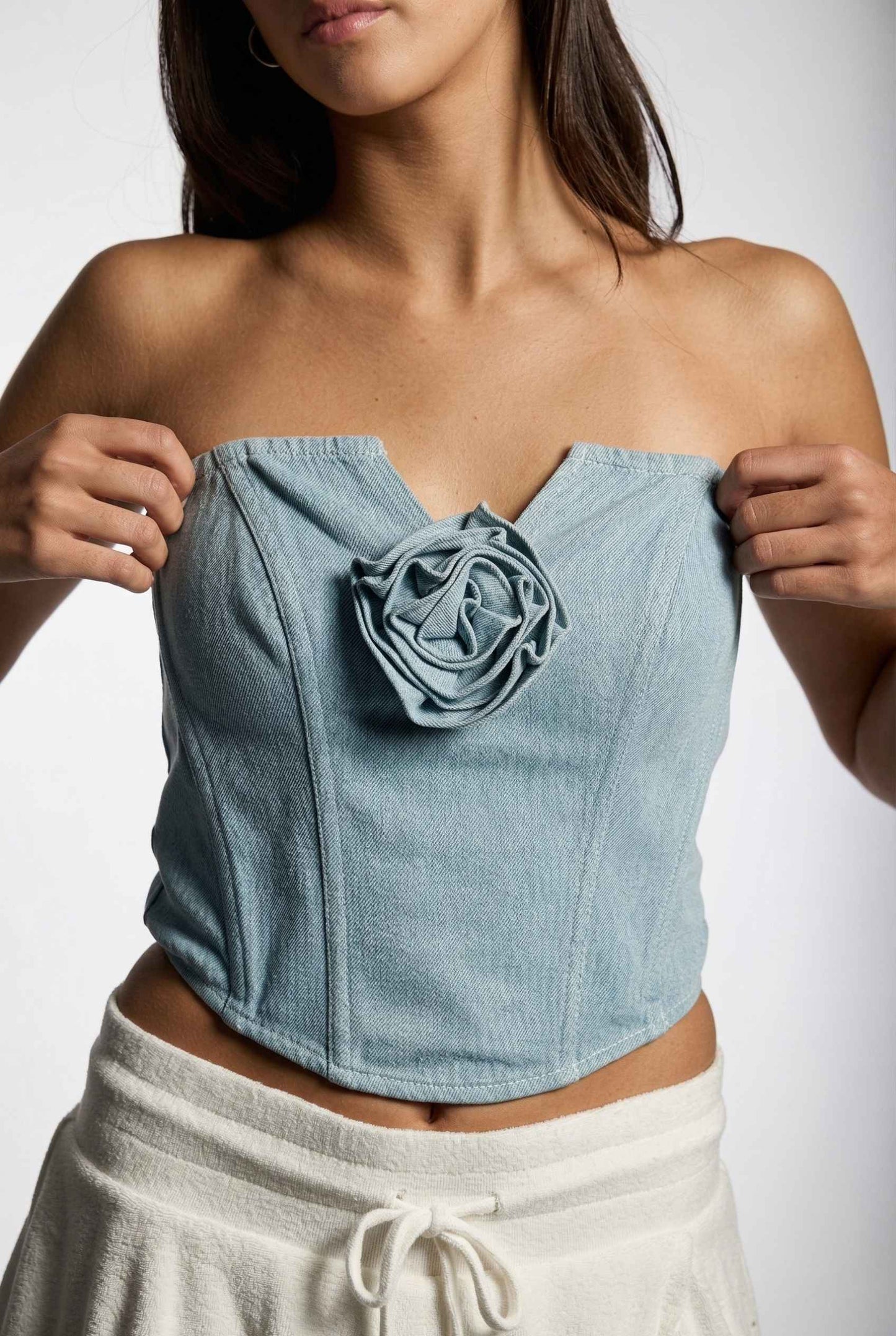 Model wearing Odette Top in Light Denim Cotton Strapless Rosette Bustier with ruffled mini skirt close up rosette detail