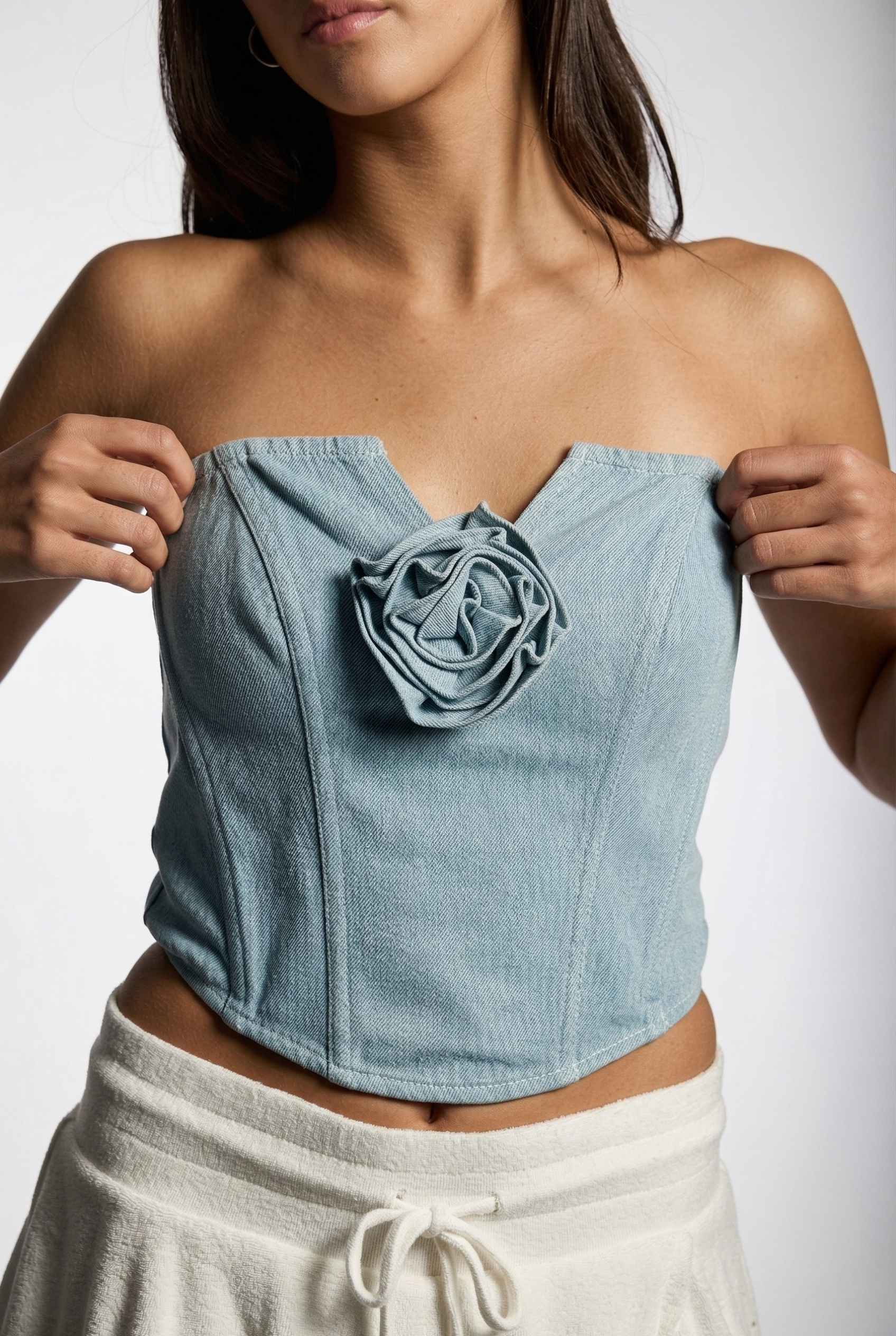 Model wearing Odette Top in Light Denim Cotton Strapless Rosette Bustier with ruffled mini skirt close up rosette detail