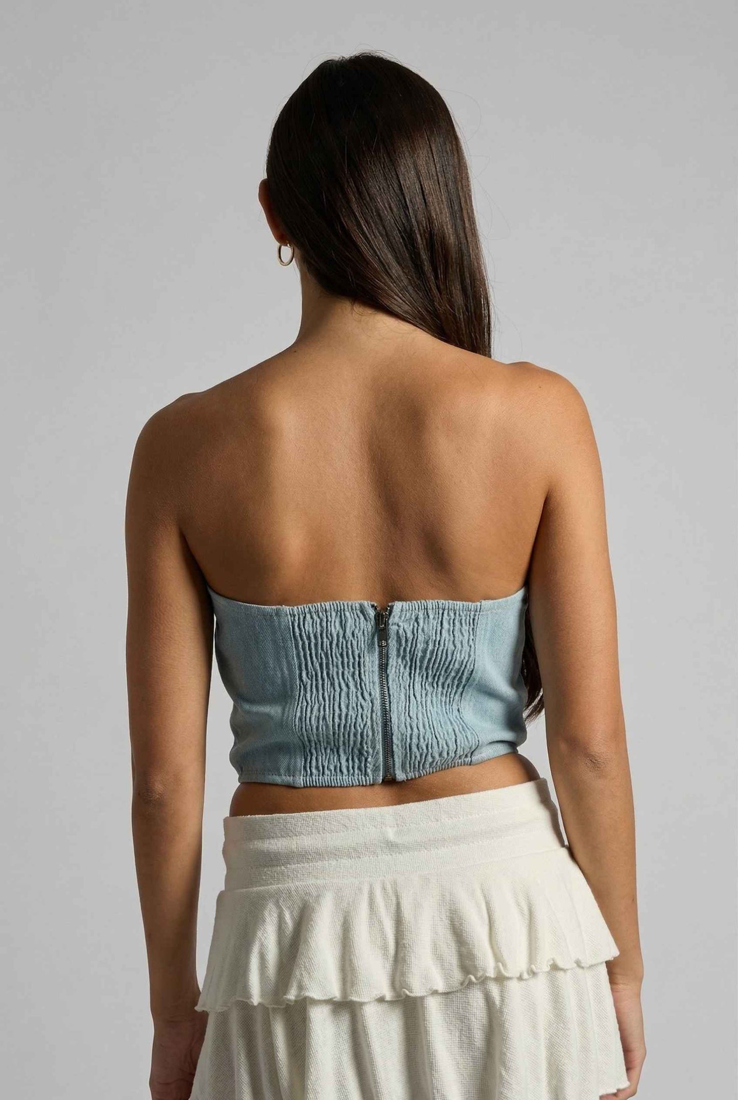 Model wearing Odette Top in Light Denim Cotton Strapless Rosette Bustier with ruffled mini skirt