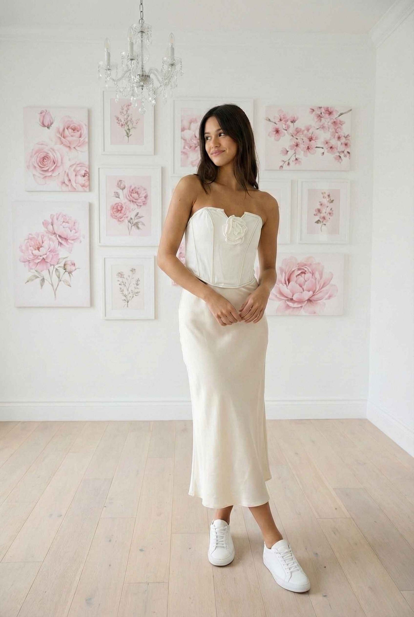 Model wearing Odette Top in White Cotton Denim Strapless Rosette Bustier with satin midi skirt and sneakers posing in chandelier room